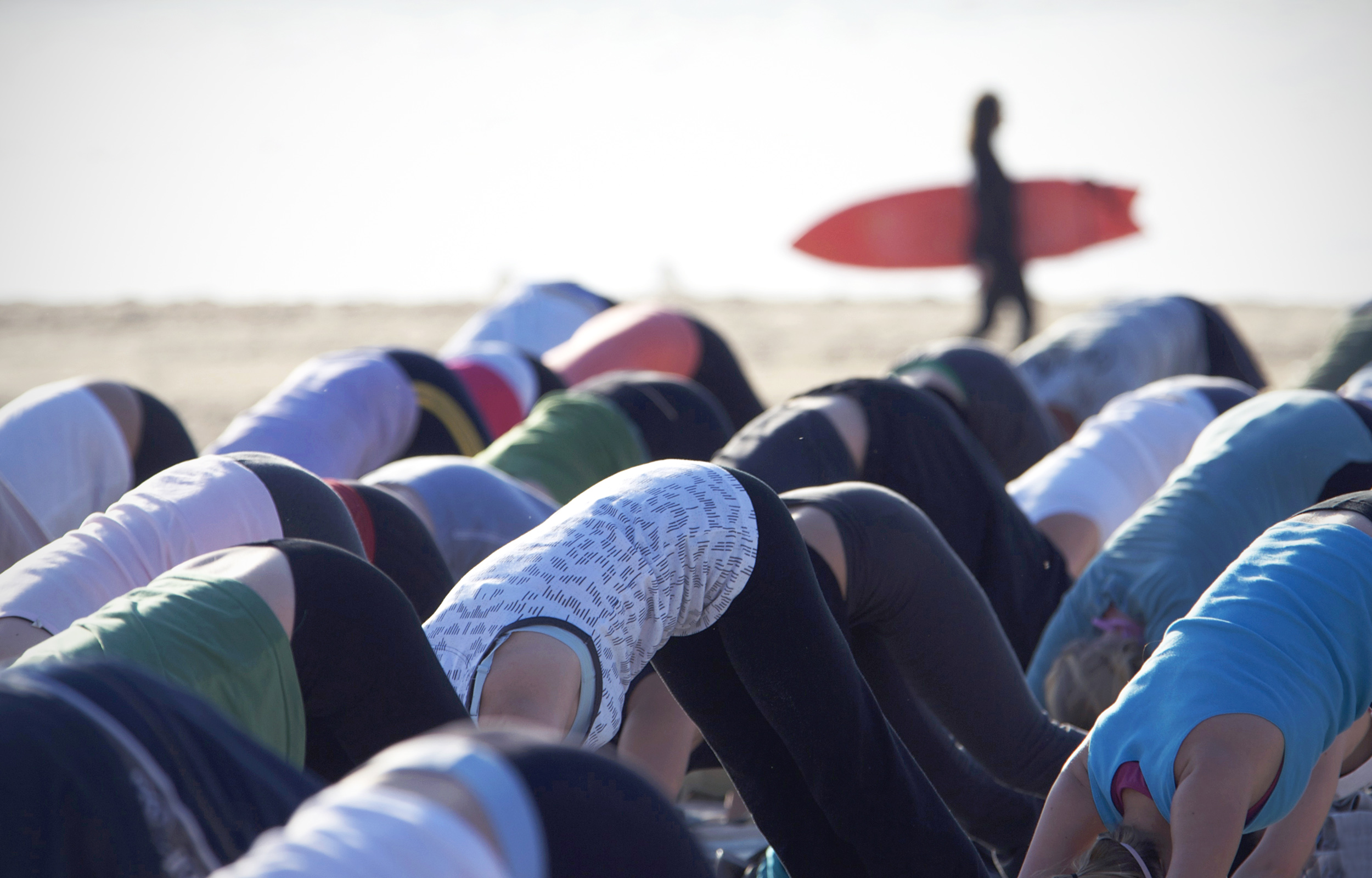 Group of ladies doing downward dog yoga pose on the beach, surfer in background, Bondi Beach, Sydney