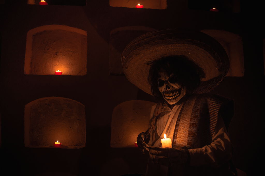 Person dressed as Santa Muerte (Death) using traditional poncho and regional hat; tombs are in the wall Photo by Misael Abad Flores