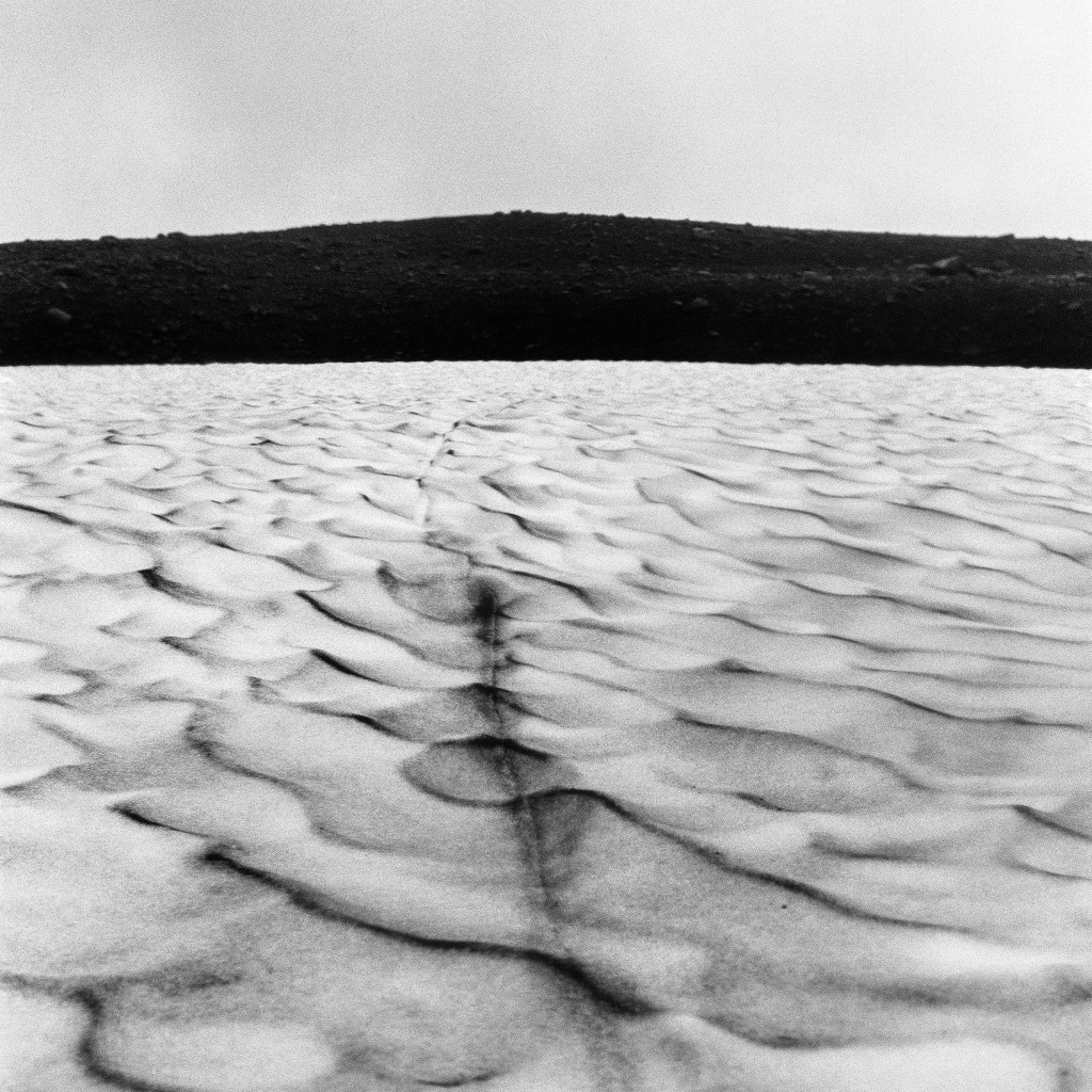 Flat expanse of ice frozen in a wave pattern meeting black desert in the disance