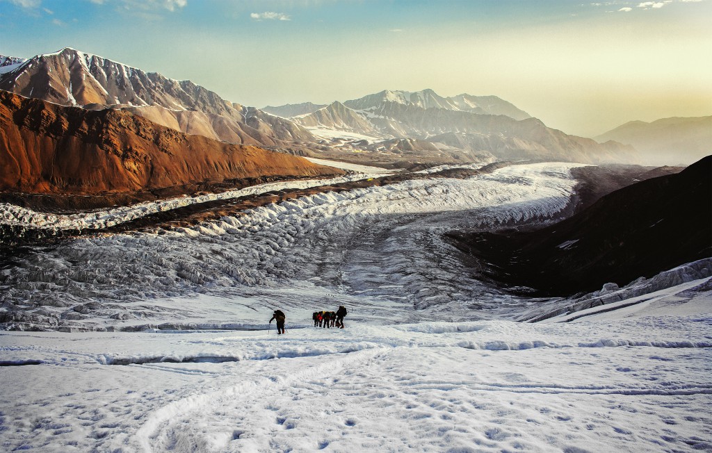 Two men and two horses trudging through the snowy landscape at sunrise near Lenin Peak