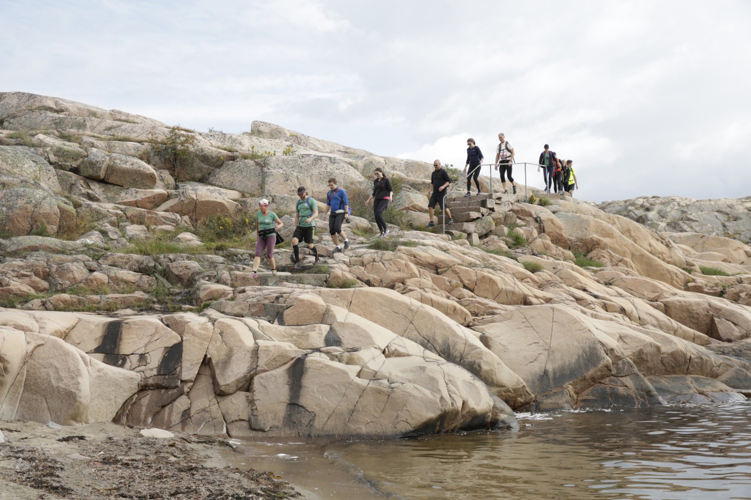 Runners running over rocks down to the water's edge on the Icebug Xperience marathon