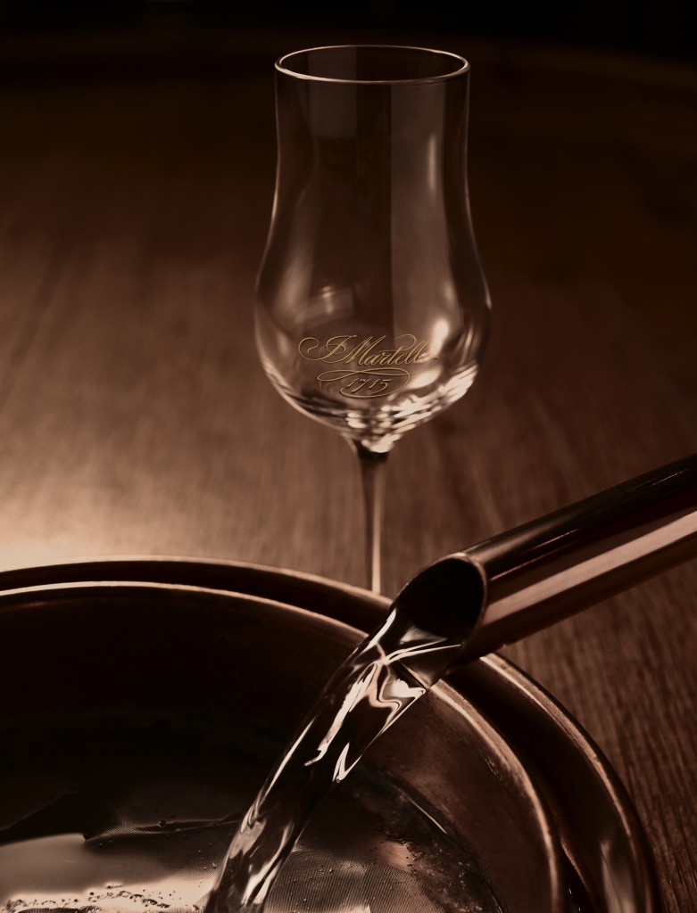 A spout pouring a distillate into a container with a wine glass to the side in Gallienne distillery, Cognac