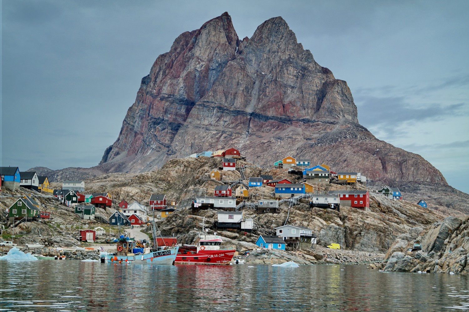 The colourful houses of Sisimut perched up a hillside with a couple of colourful boats at the water's edge, Greenland