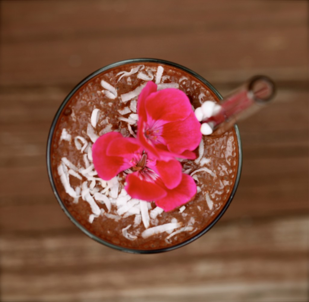 View from above of a Jamaican mocha teeccino in a glass with straw topped with shredded coconut and a red flower