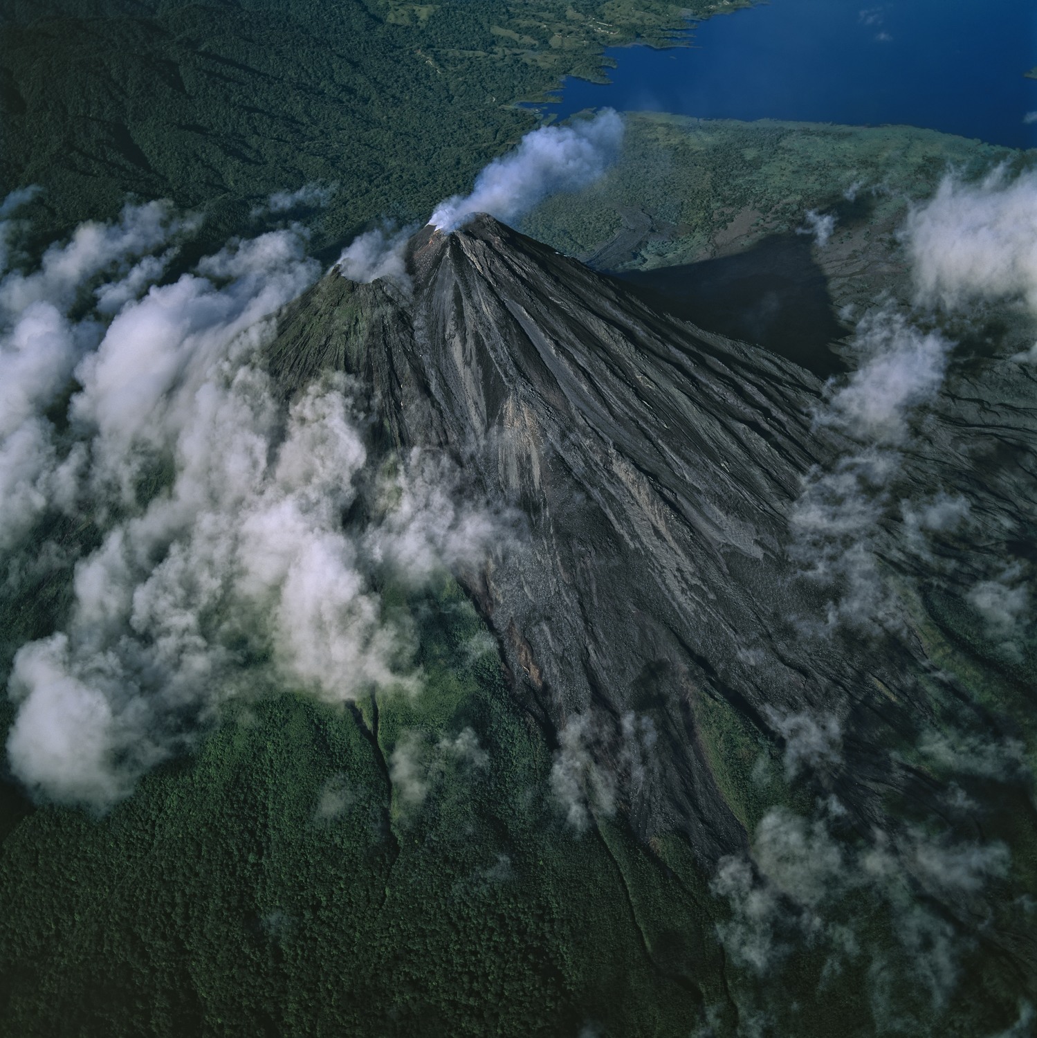 A aerial view of the conical Arenal Volcano wreathed in clouds with smoke emanating from its tip in Costa Rica 