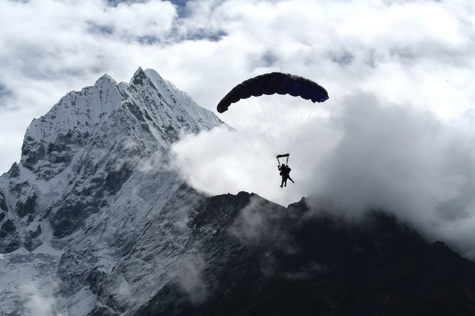 Two skydivers strapped together and silhouetted against clouds with Mt Everest in the background