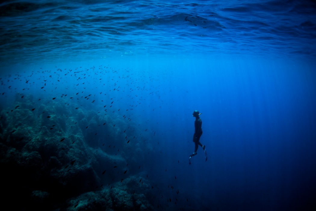 A freediver ascending vertically through the deep blue waters of Villefranche-sur-Mer, Nice, France