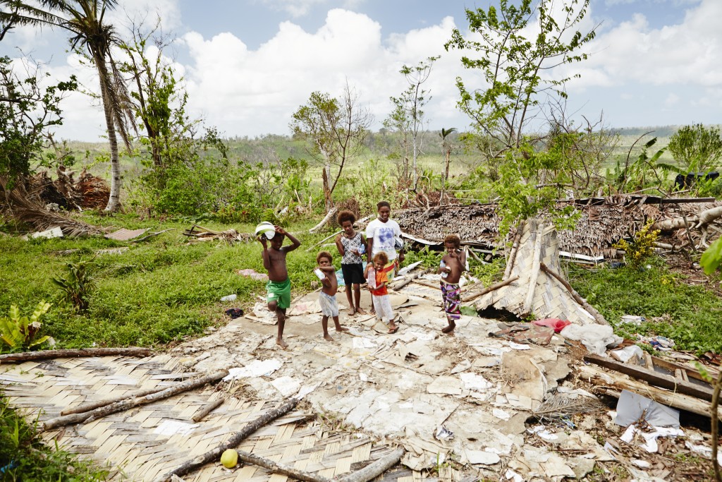 A family stand on their cyclone-flattened home, Vanuatu. Photo by Matt Crawford