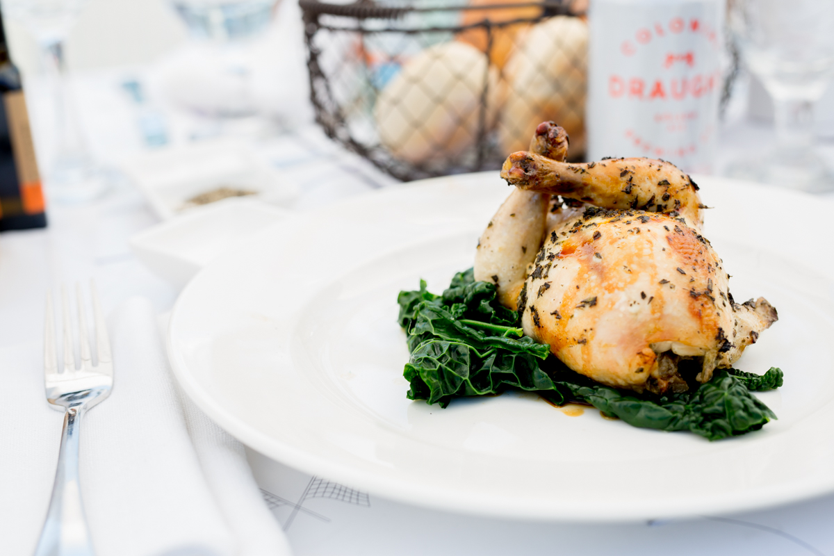 A roast chicken in a bed of wilted spinach on a plate on a dressed table with a fork beside it