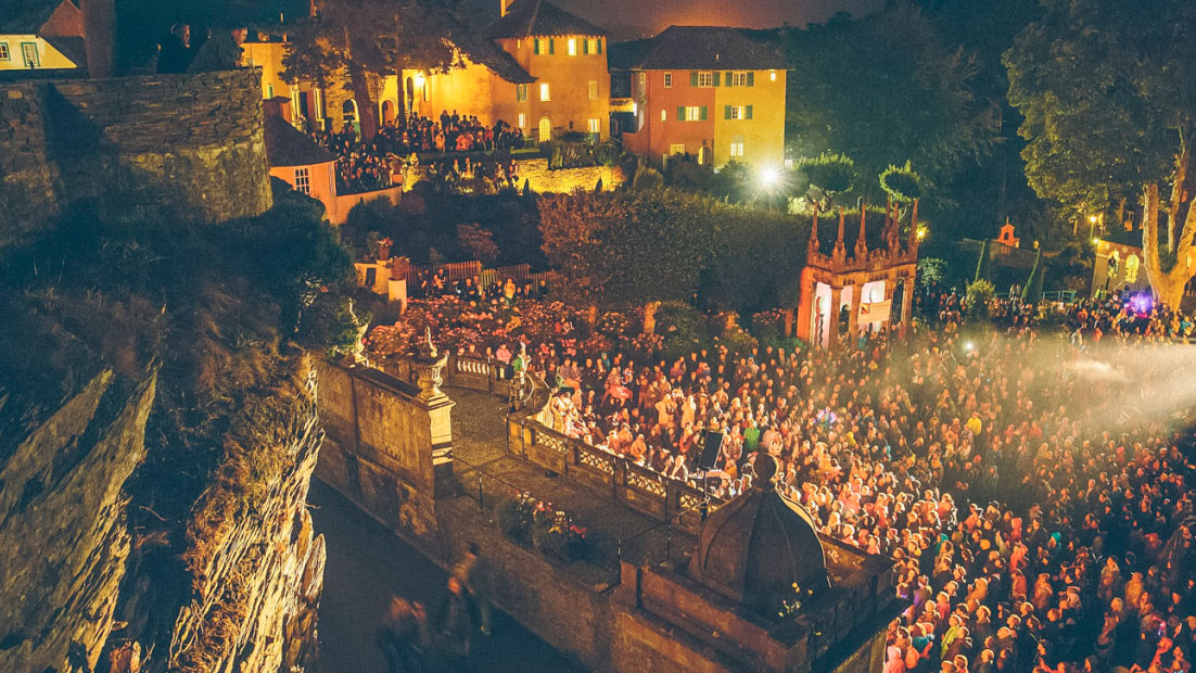 Crowd watching a performance at night with town buildings bathed in light at Festival No. 6, Wales