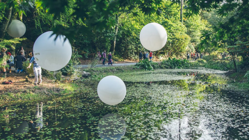 White balloons suspended over a green pond for Festival No 6