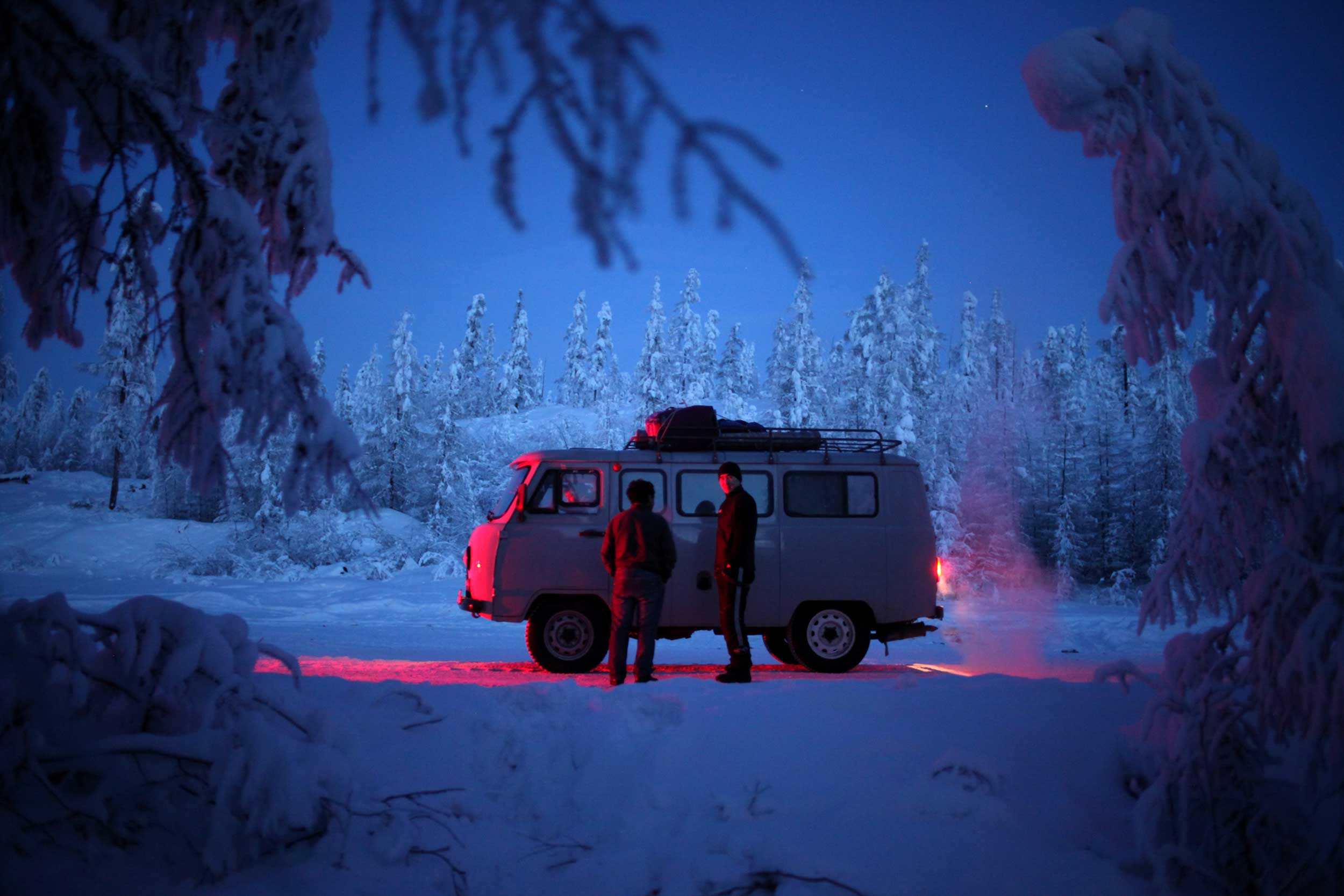 Two men by a van in a snowy forest in Oymyakon which is the coldest inhabited place