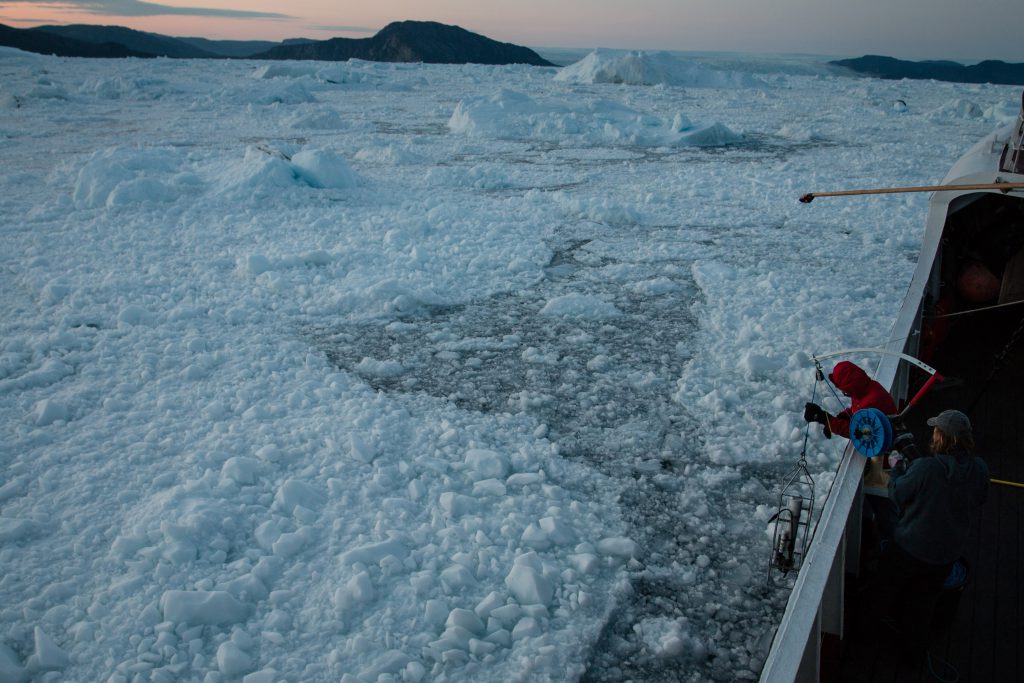 Researchers lowering a measuring device into the icy sea off west Greenland.