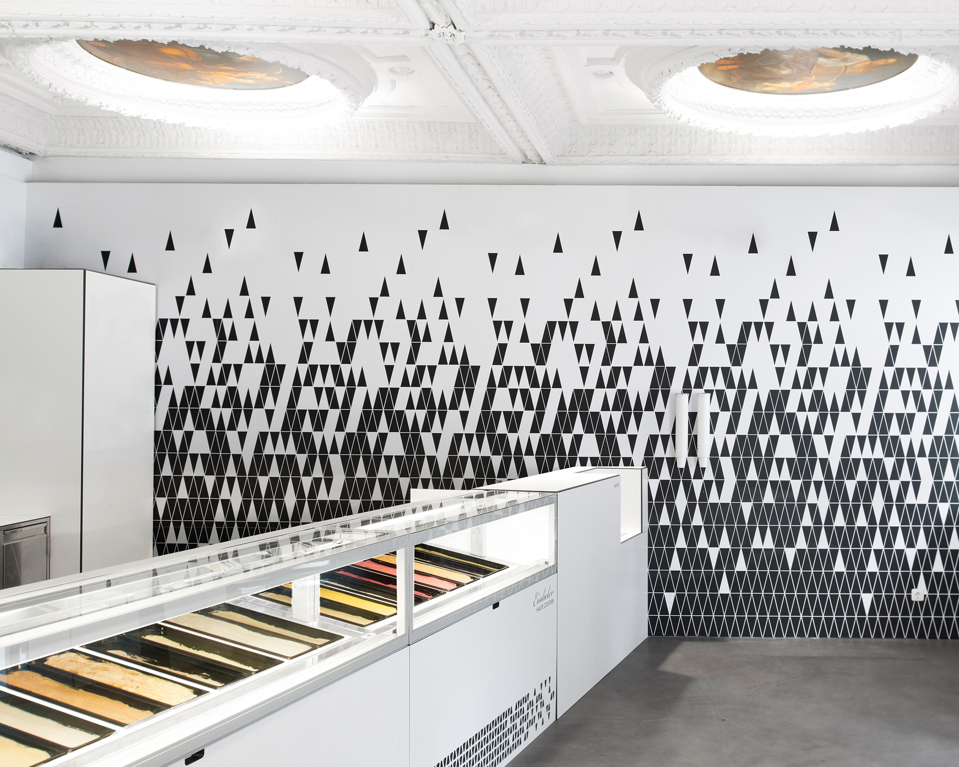An ice cream display case in a parlour with a black and white patterned wall at the end of it in Eisdieler, Austria