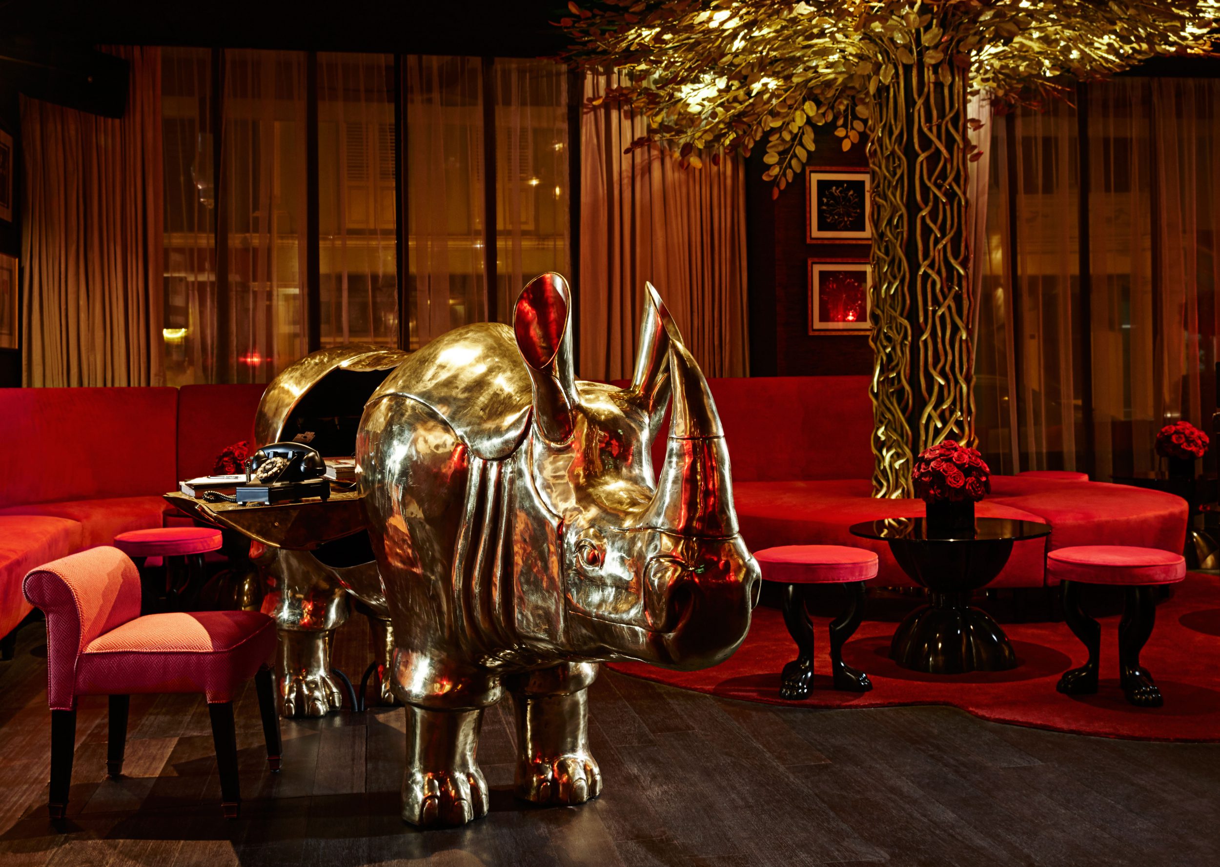 A brass rhino with a table built into its middle in the plush red reception of Hotel Vagabond, Singapore