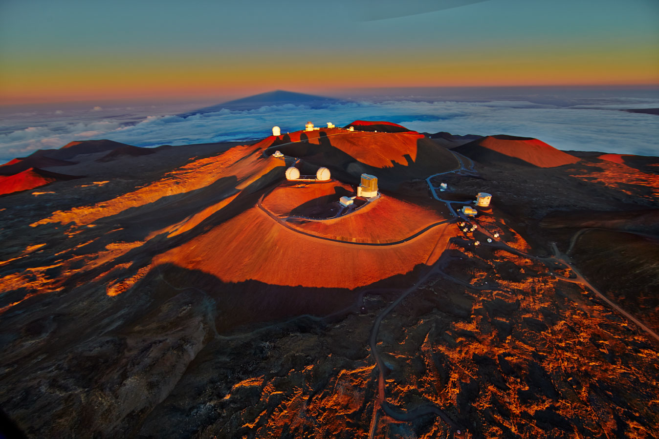 An aerial view of observatories and telescopes on a mountaintop in a very orange sunset at Mauna Kea, Hawai'i