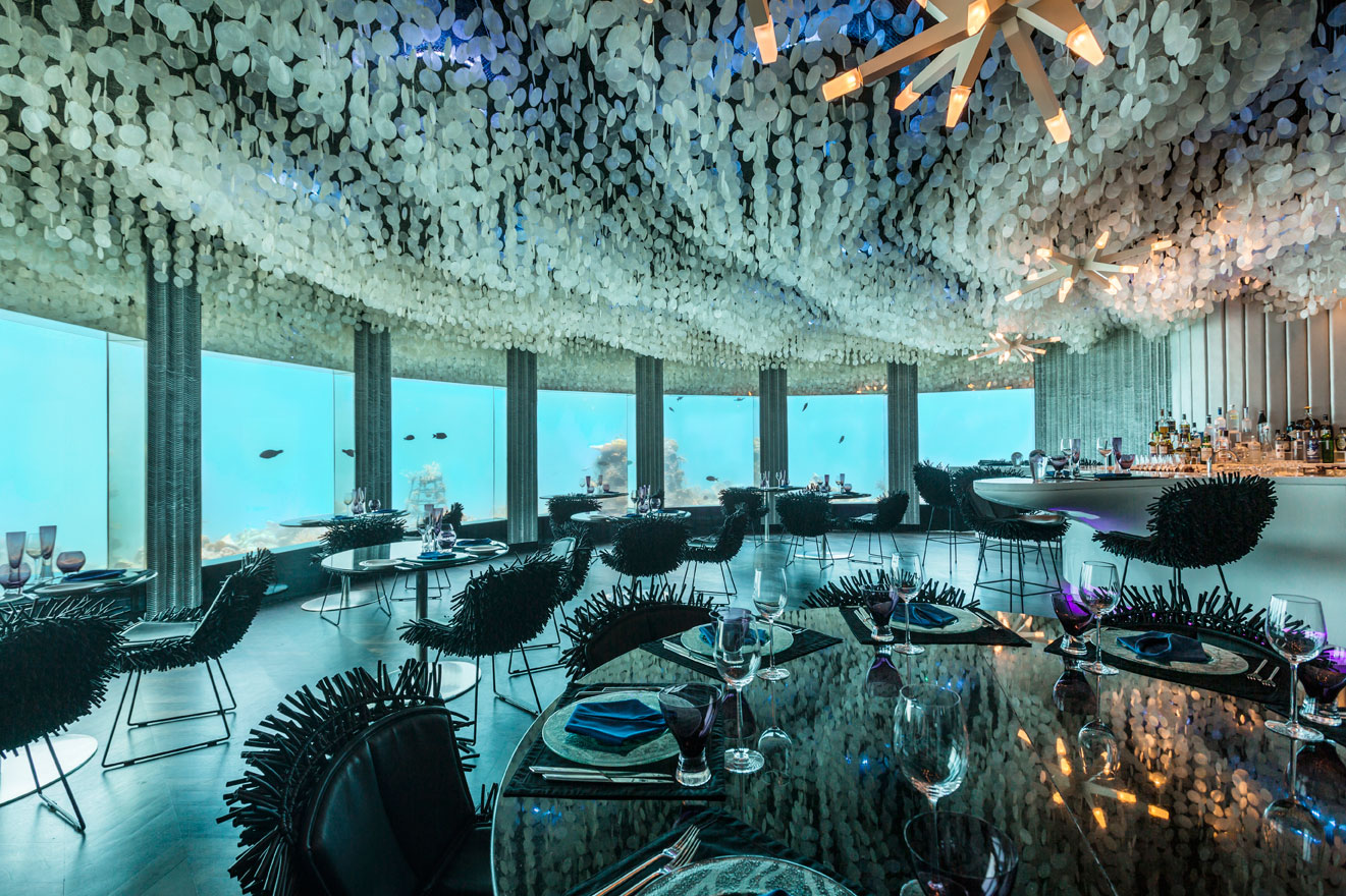 View over the underwater restaurant's tables and chairs to plate glass windows and seeing fish and coral, Niyama, Maldives
