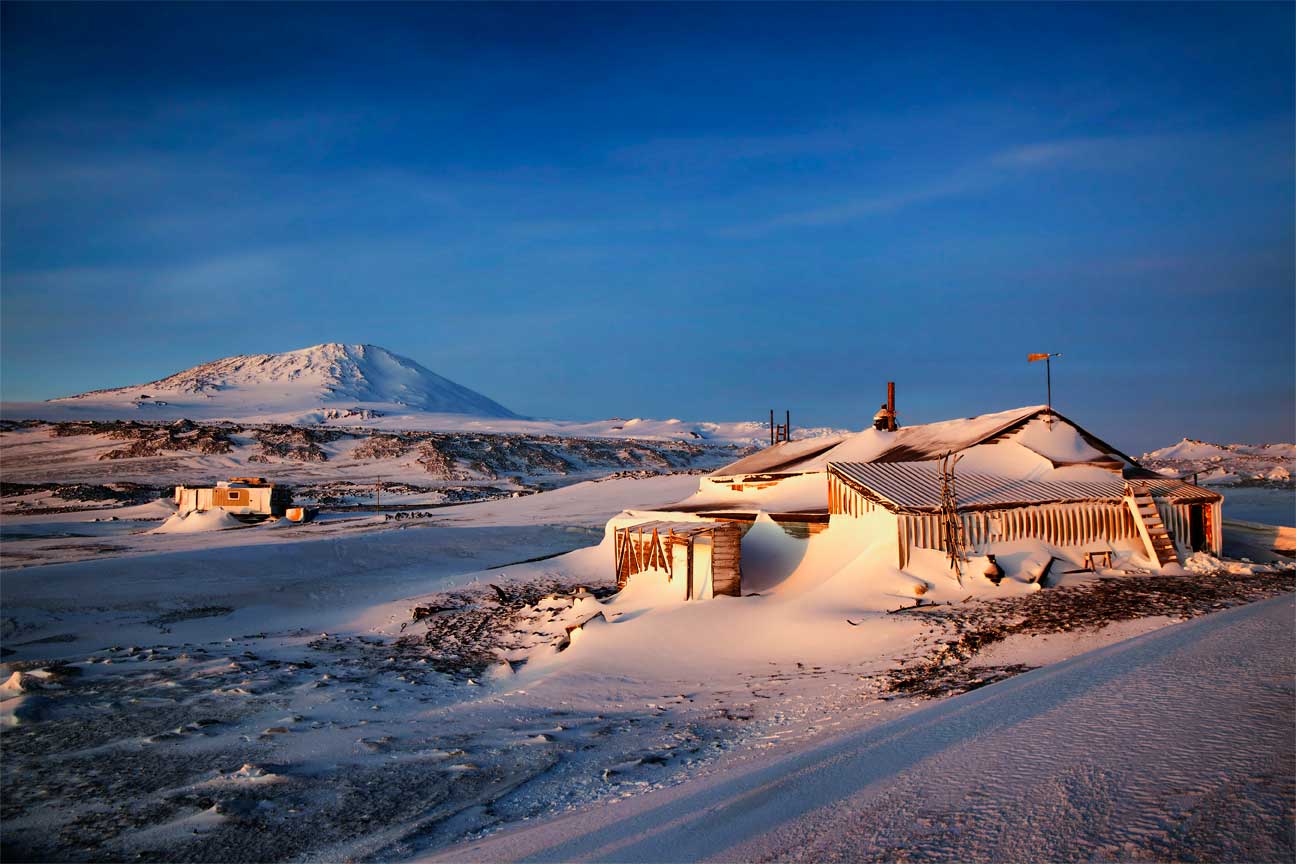 Wild World: View of two dwellings on the snowy landscape of Antarctica with Mt Erebus in the distance