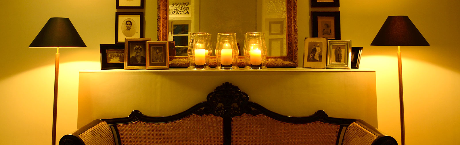Framed photos on a mantlepiece above a couch with lighted lamps on either side at Maniumpathy Boutique Hotel, Colombo, Sri Lanka