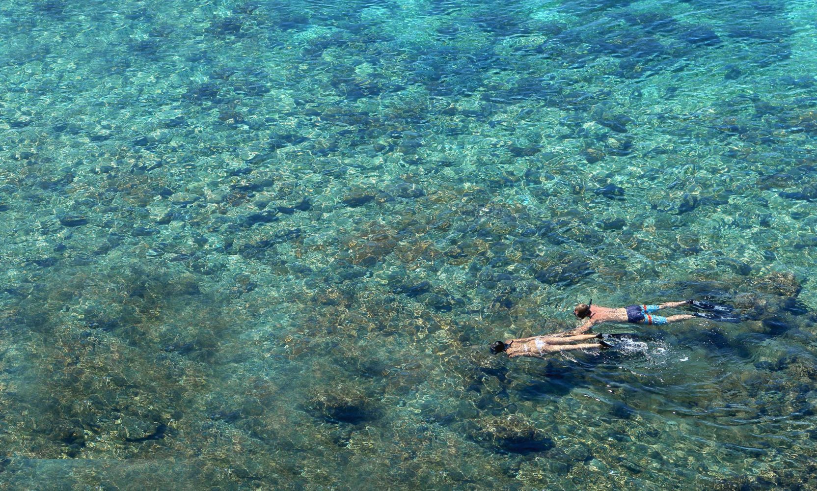 Aerial view of a couple snorkelling in a very shallow and clear blue sea