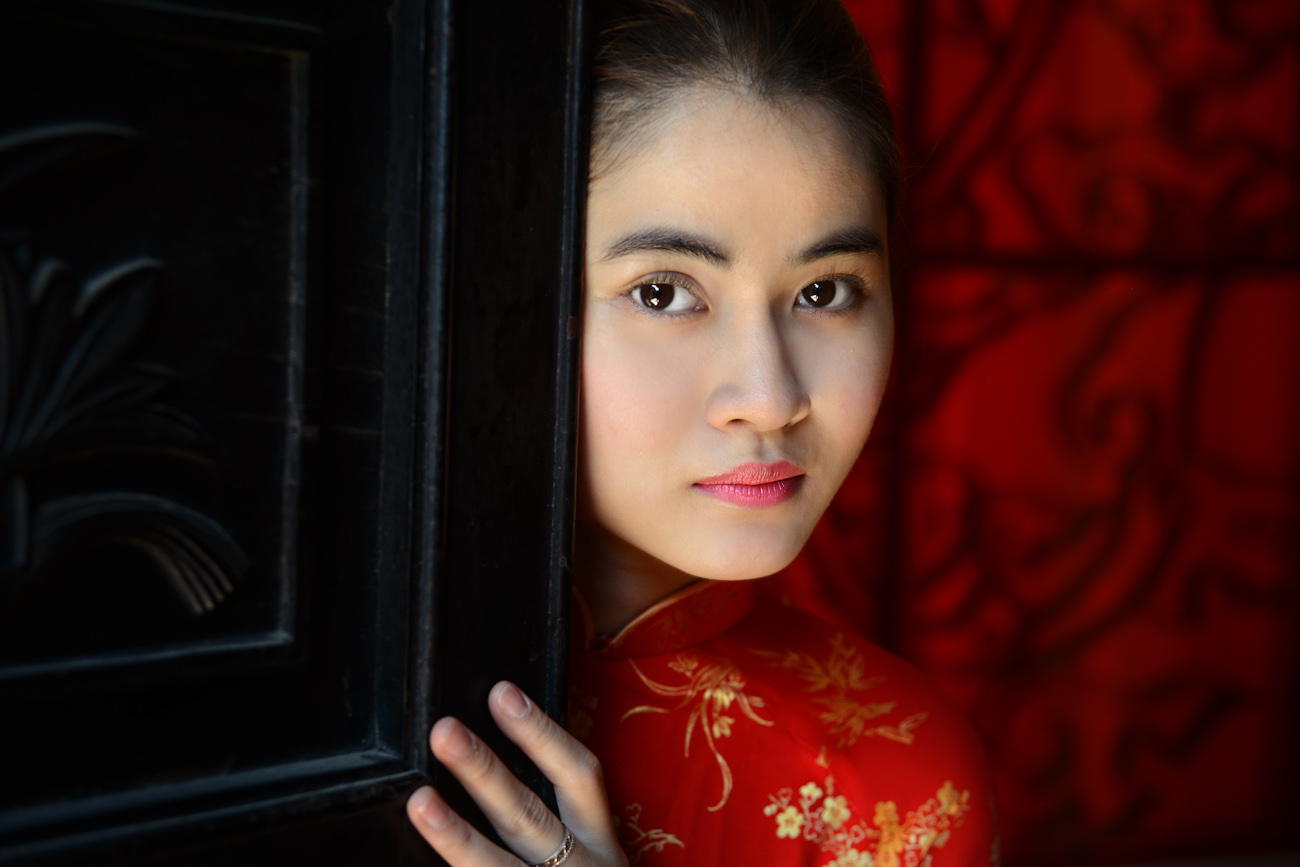 Girl dressed in red peering round a door, Saigon