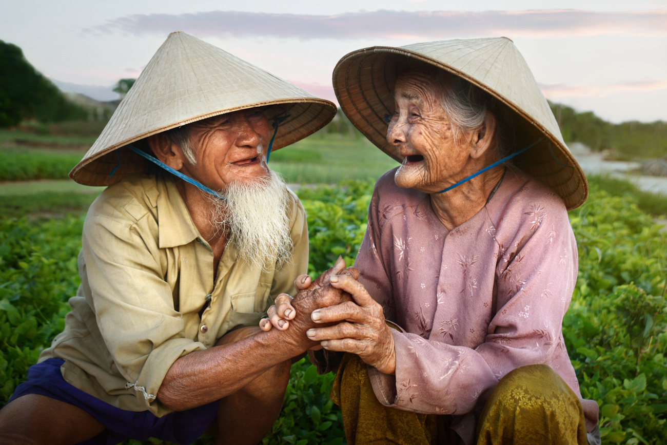 An old couple laughingly hold hands while sitting in their garden