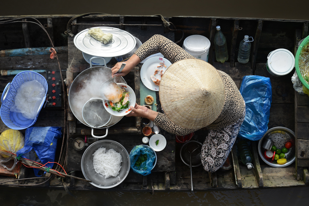 Aerial view of a local woman cooking in her small boat with utensils and food around her