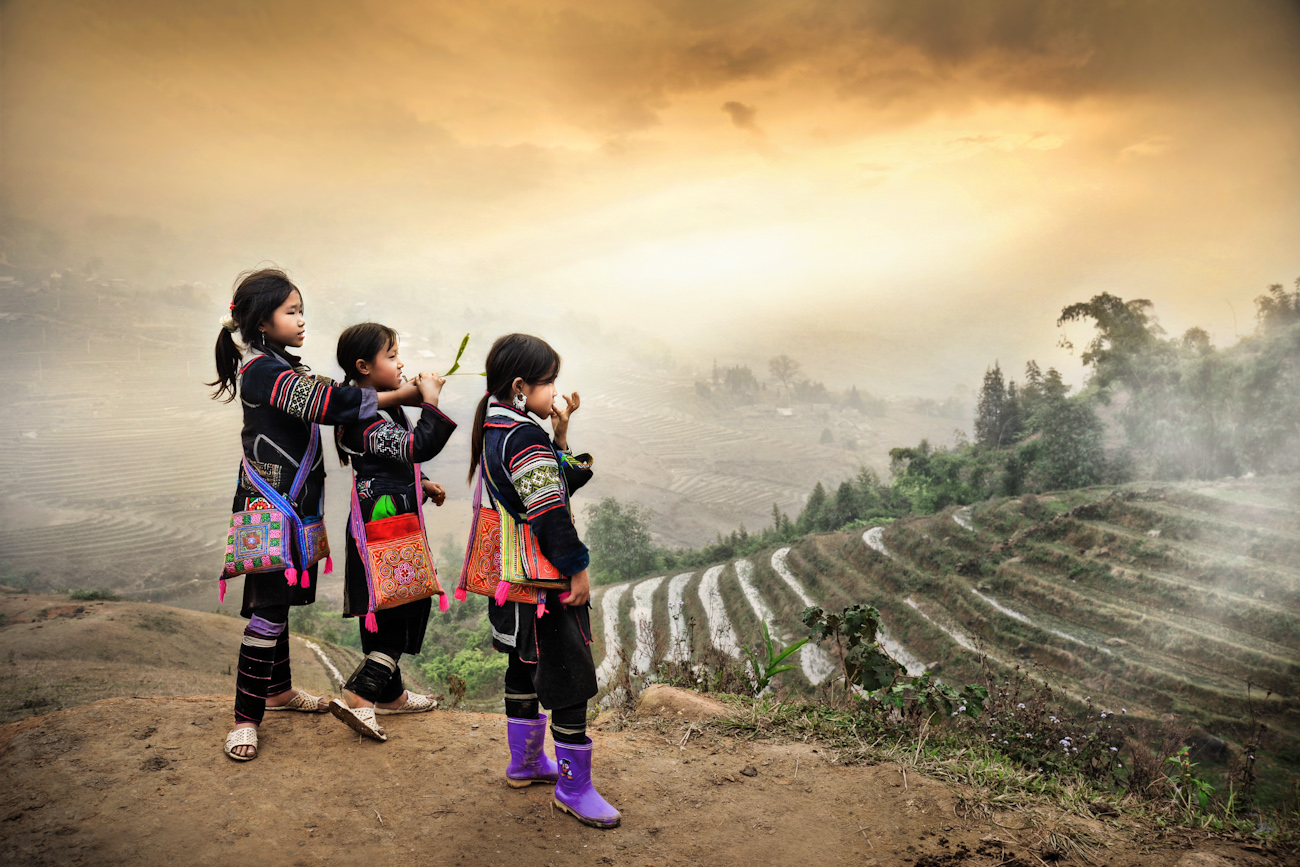 Three girls in traditional clothing gaze out towards mountains and rice terraces
