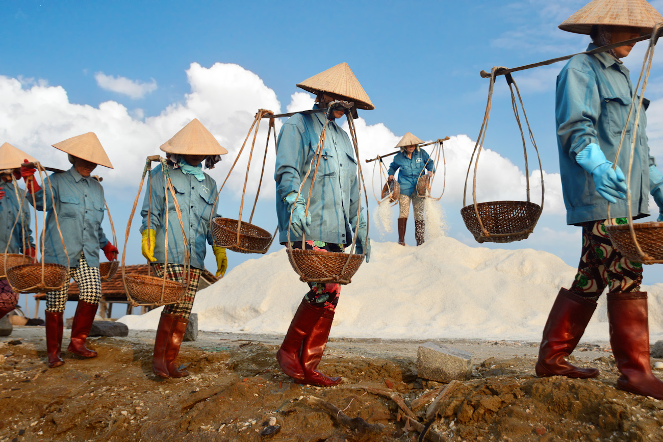 Line of women carrying baskets of salt balanced off a pole on their shoulders