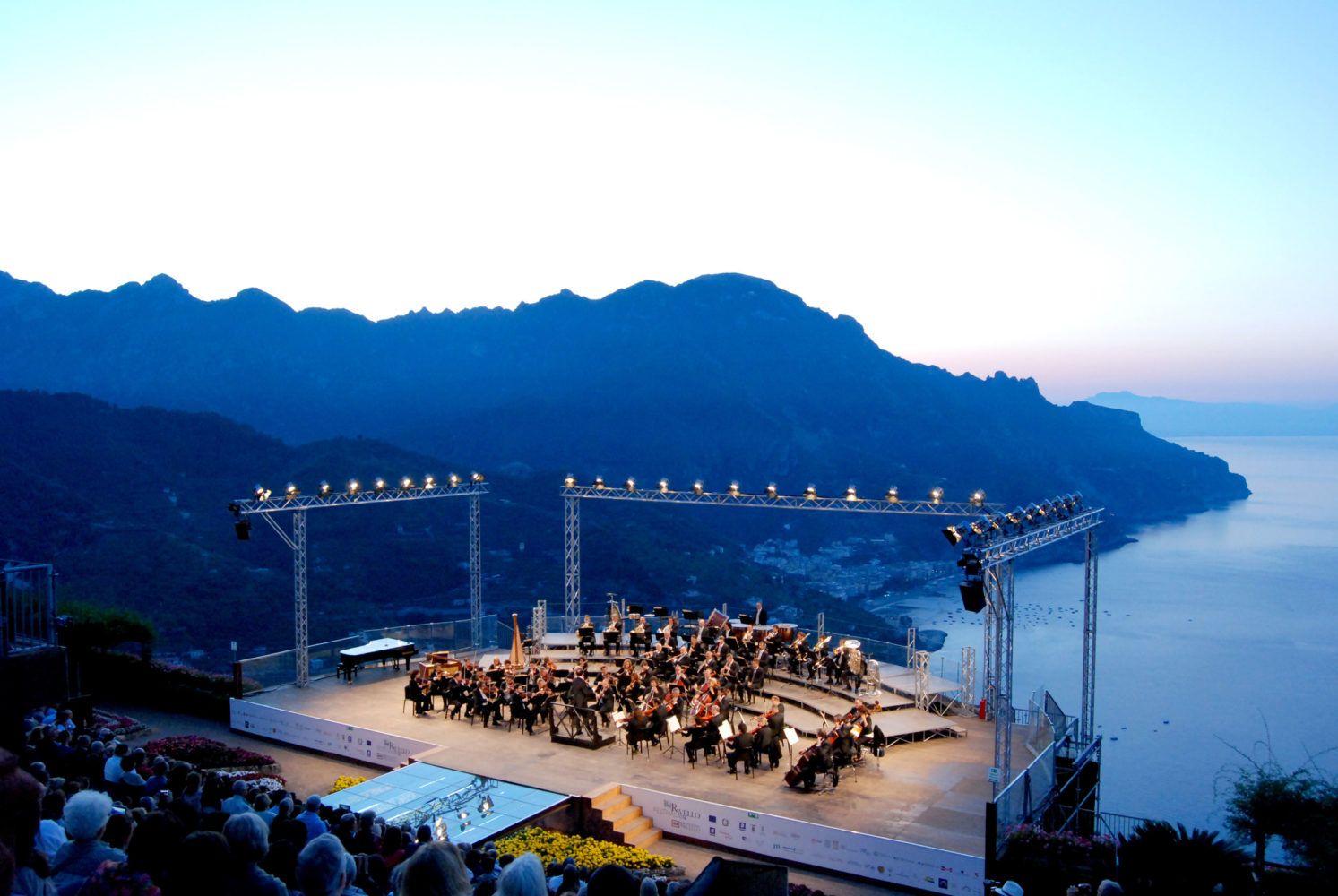 Looking down onto the crowd at an orchestra playing on the outdoor stage with the Amalfi coastline for a backdrop