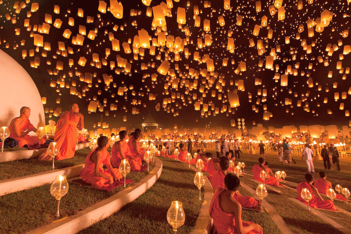 Rows of monks seated on steps watching lanterns float away into the night sky