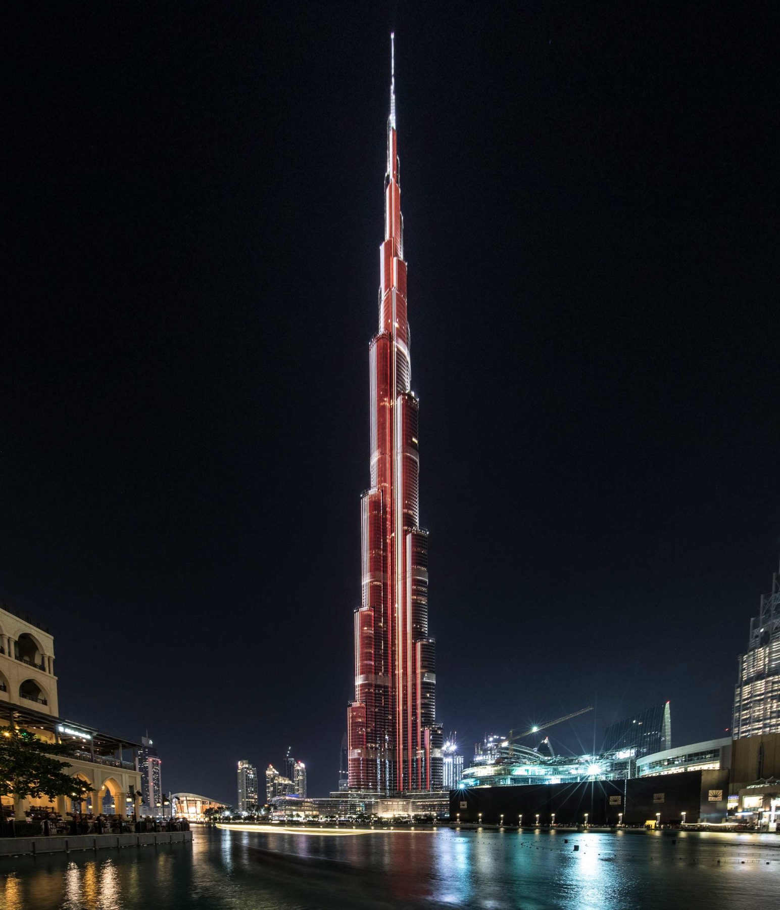 A tall, red-lighted spire of a building rising above the Dubai skyline