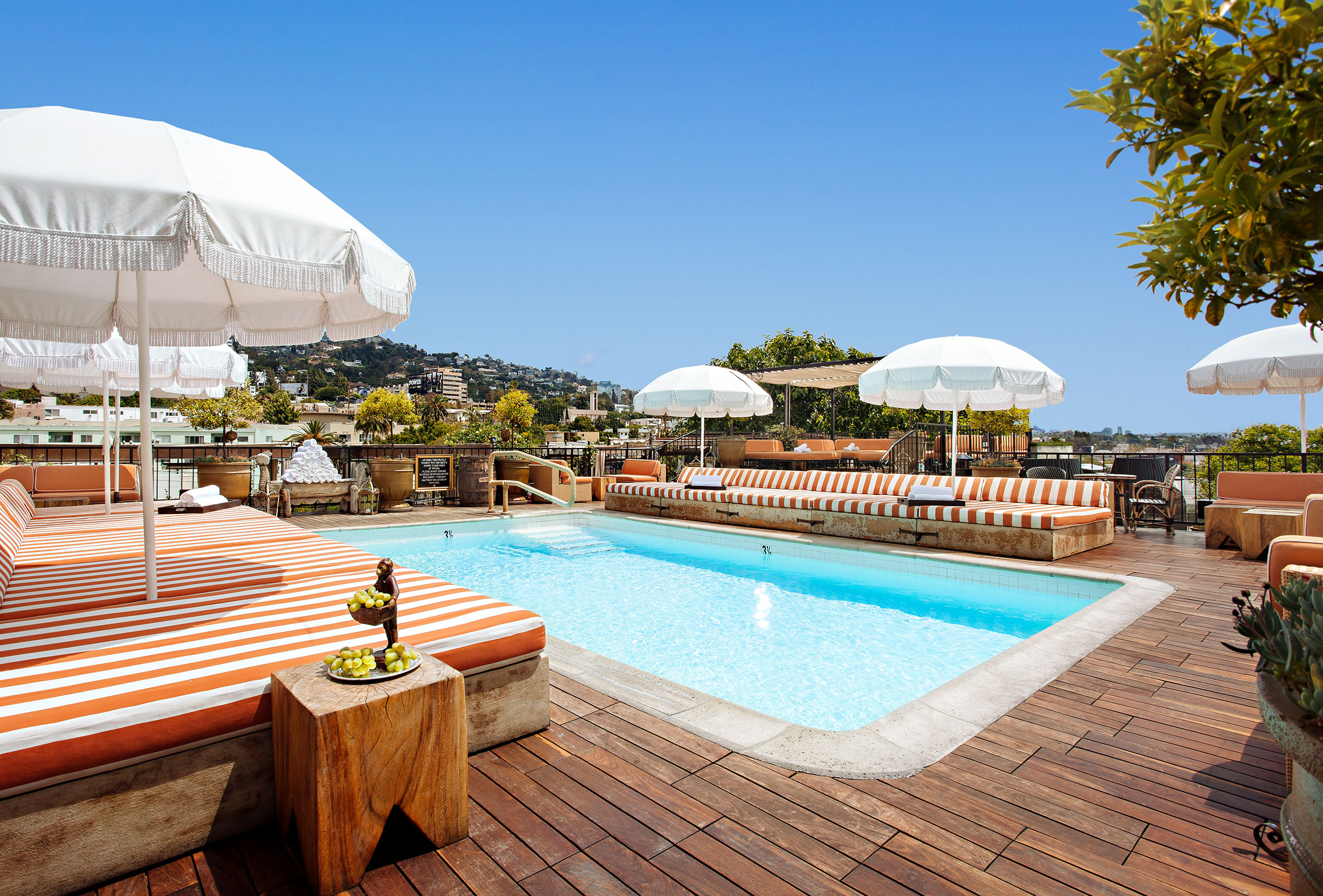 Small swimming pool surrounded by wooden decking, red and white striped sun loungers with white umbrellas