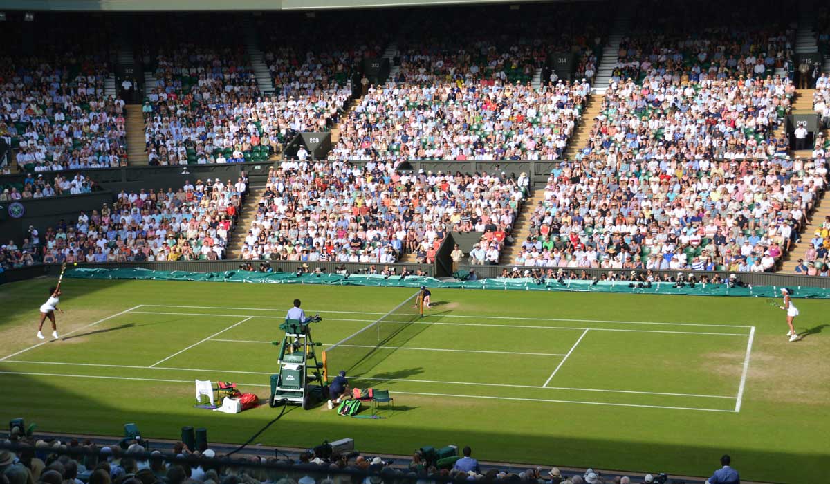Two women playing tennis singles with a packed stadium watching them