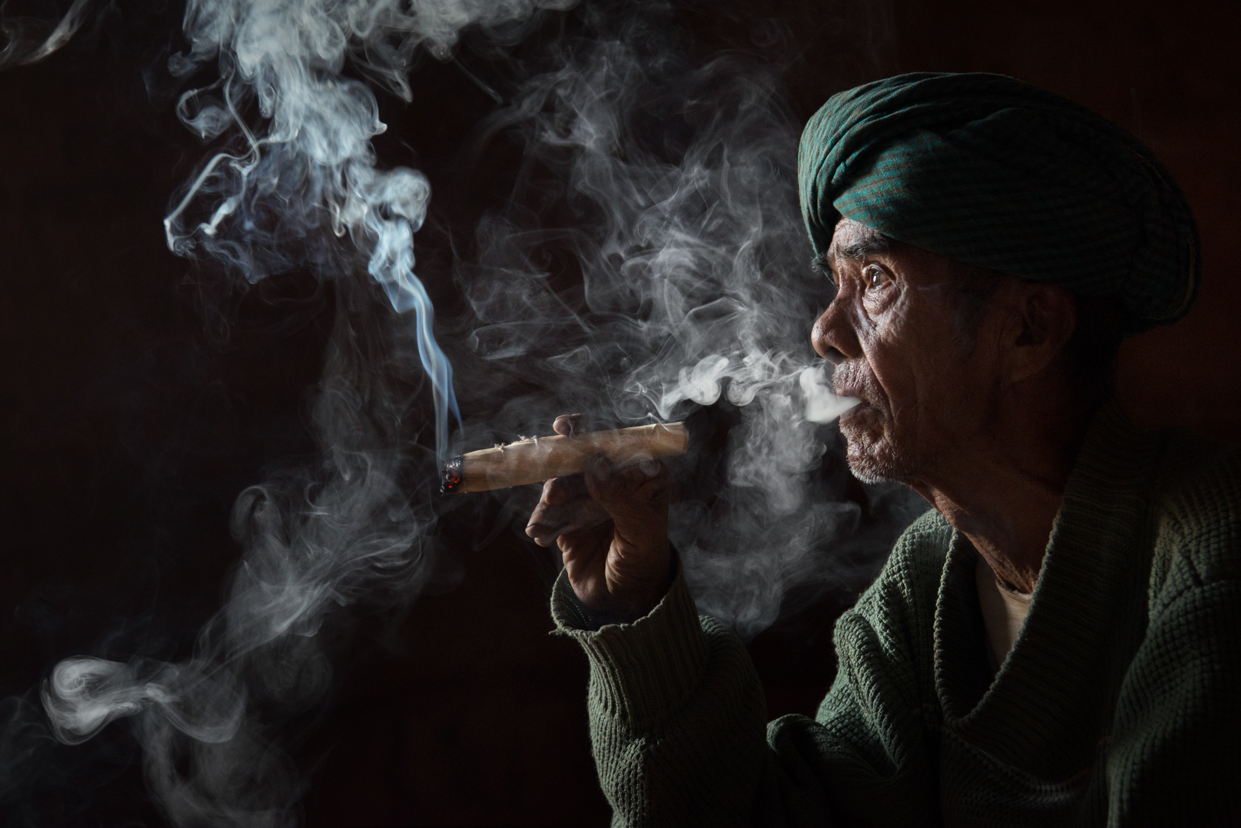 A side view of a man holding a cheroot with smoke curling off it