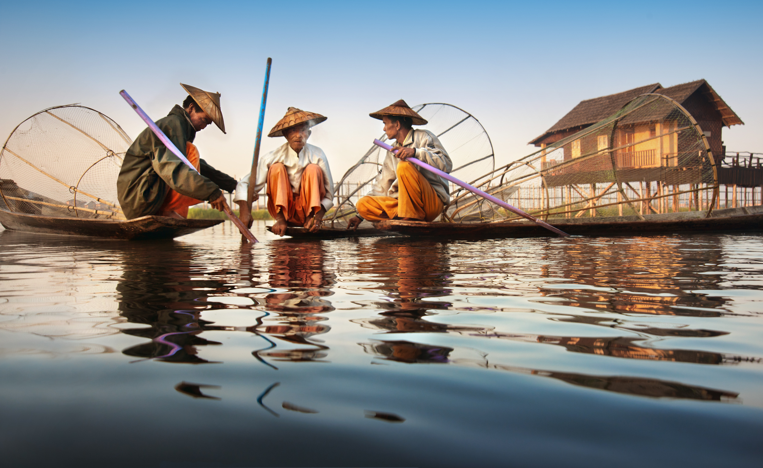 Three fishermen with conical hats squatting on their boats and chatting