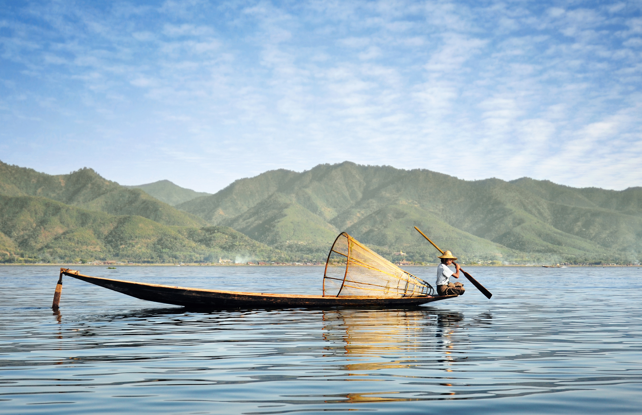 A local fisherman in Myanmar with a conical fish net on his boat in Myanmar