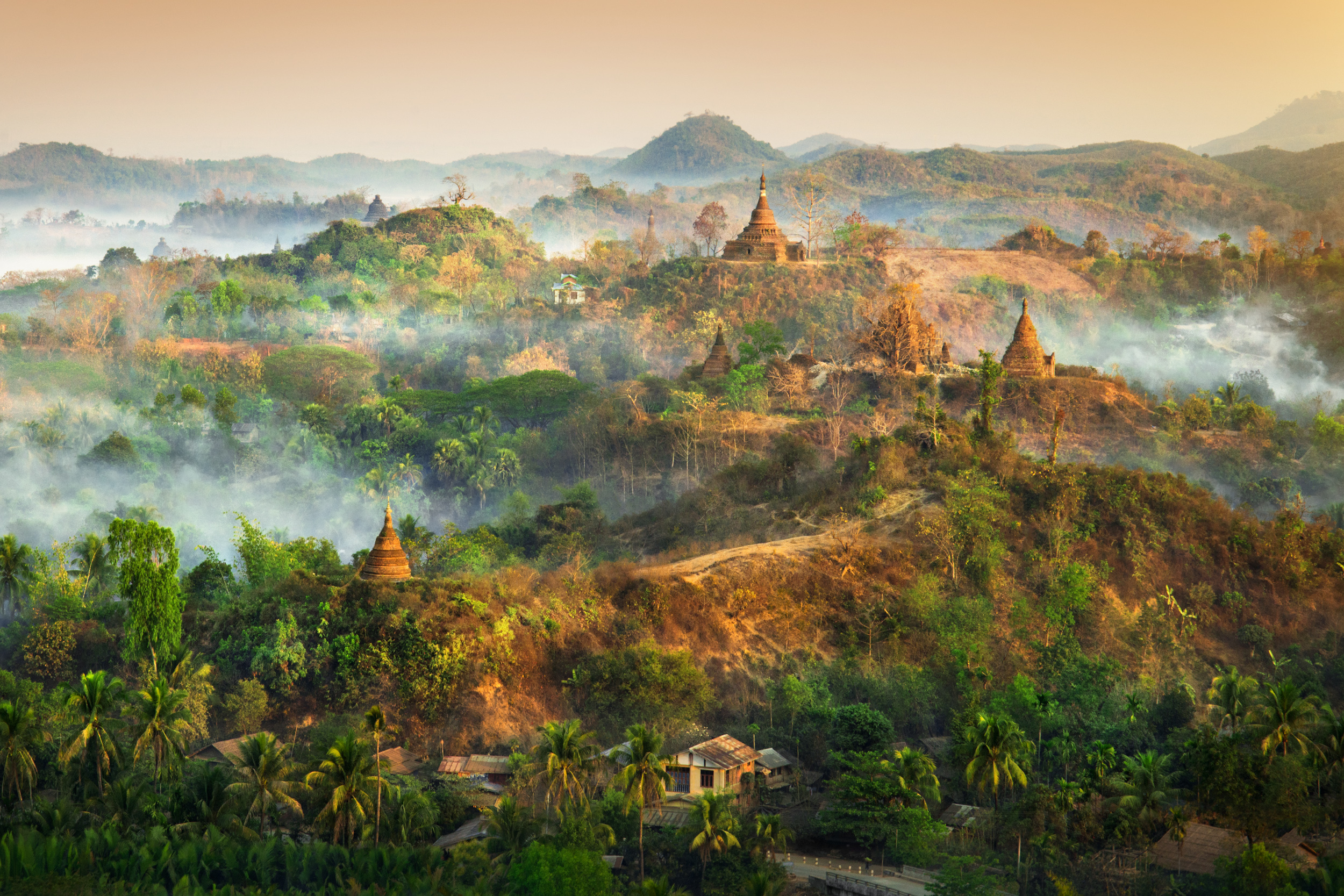 Aerial view of multiple stupas with smoke curling through them and the hills at sunrise, Myanmar