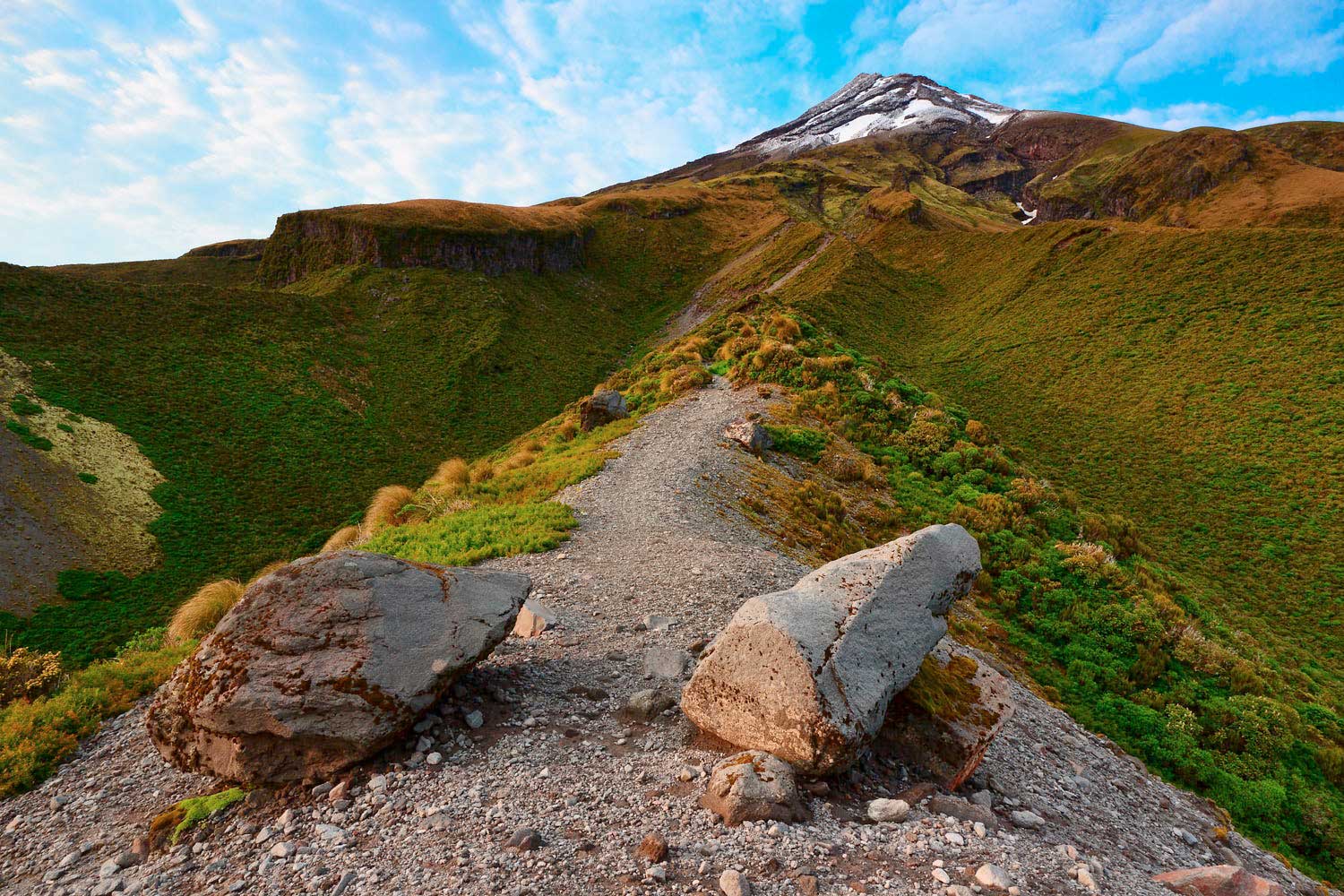 A pathway along a ridge leading up a mountainside with the peak of Mt Taranaki in the distance, Egmont National Park