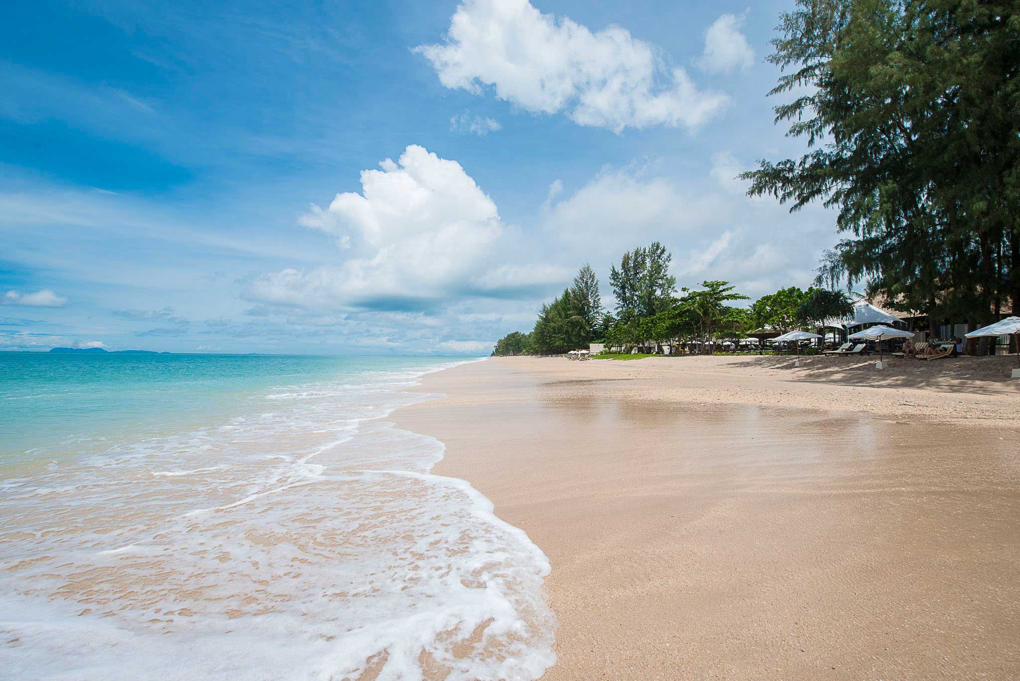 Sea foam from waves swirling up to a pristine, flat sandy beach, Thailand