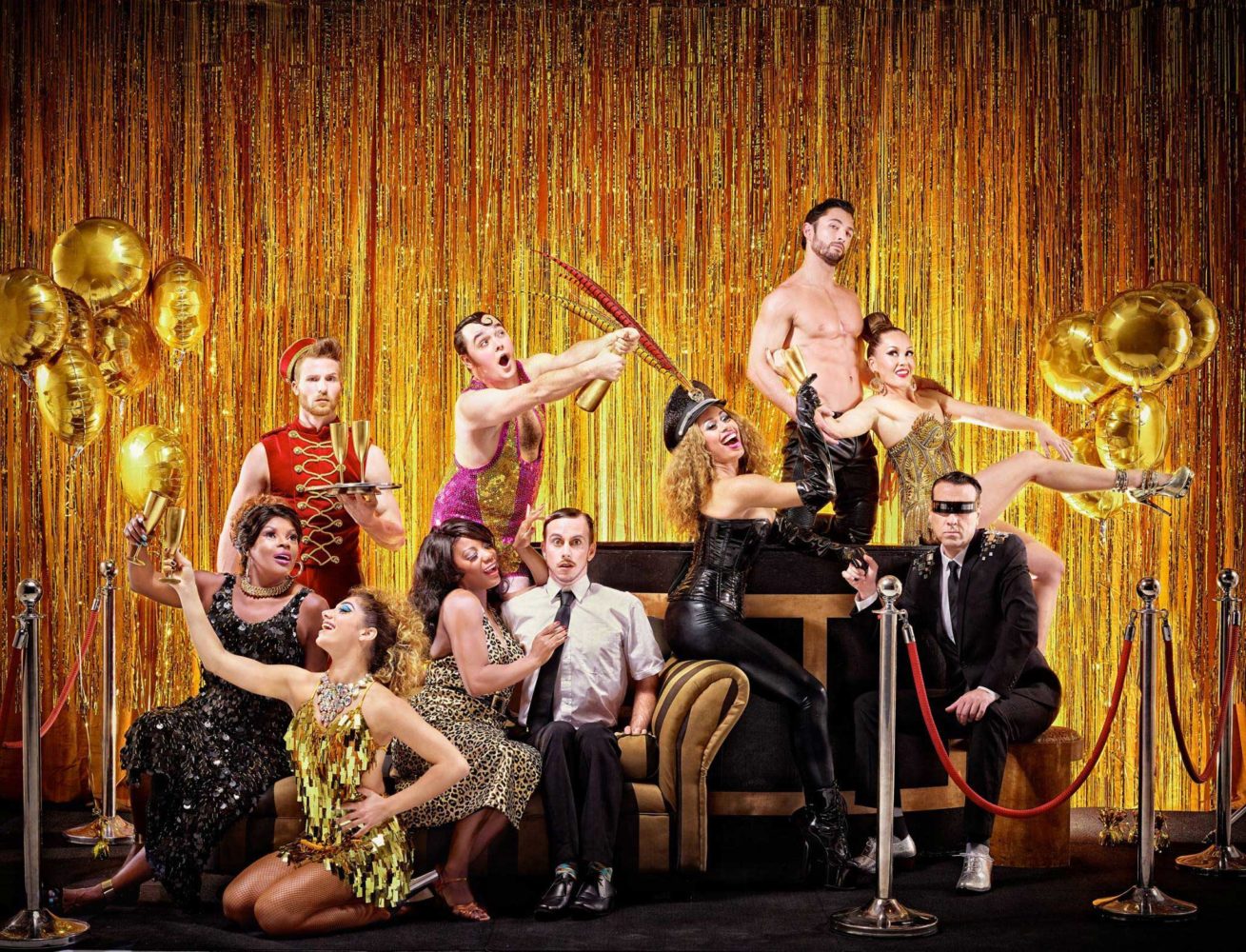 A group of vaudeville performers posed on stage with a gold-curtained backdrop