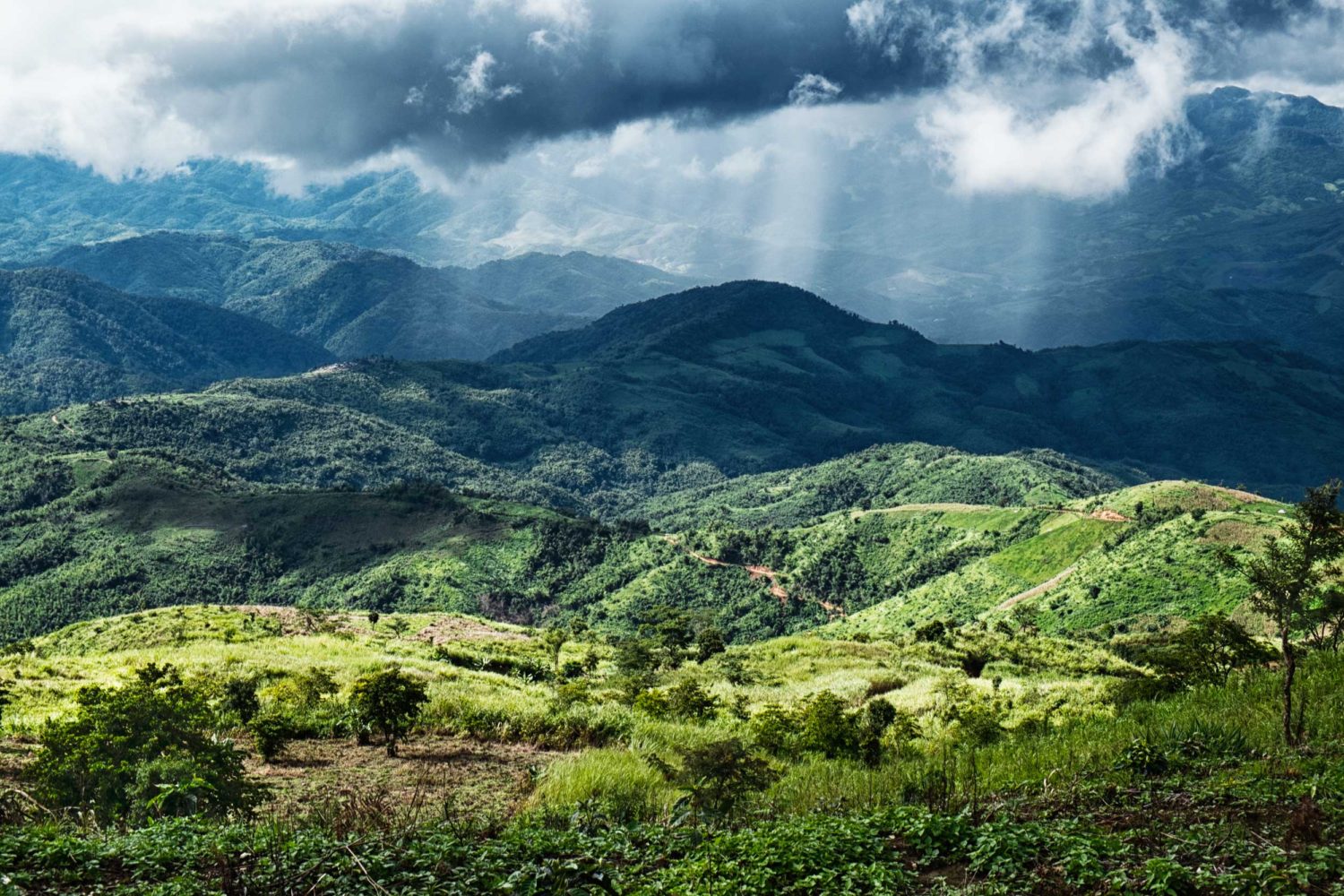View out over mountain ranges with a cloudburst above them in the distance, Myanmar