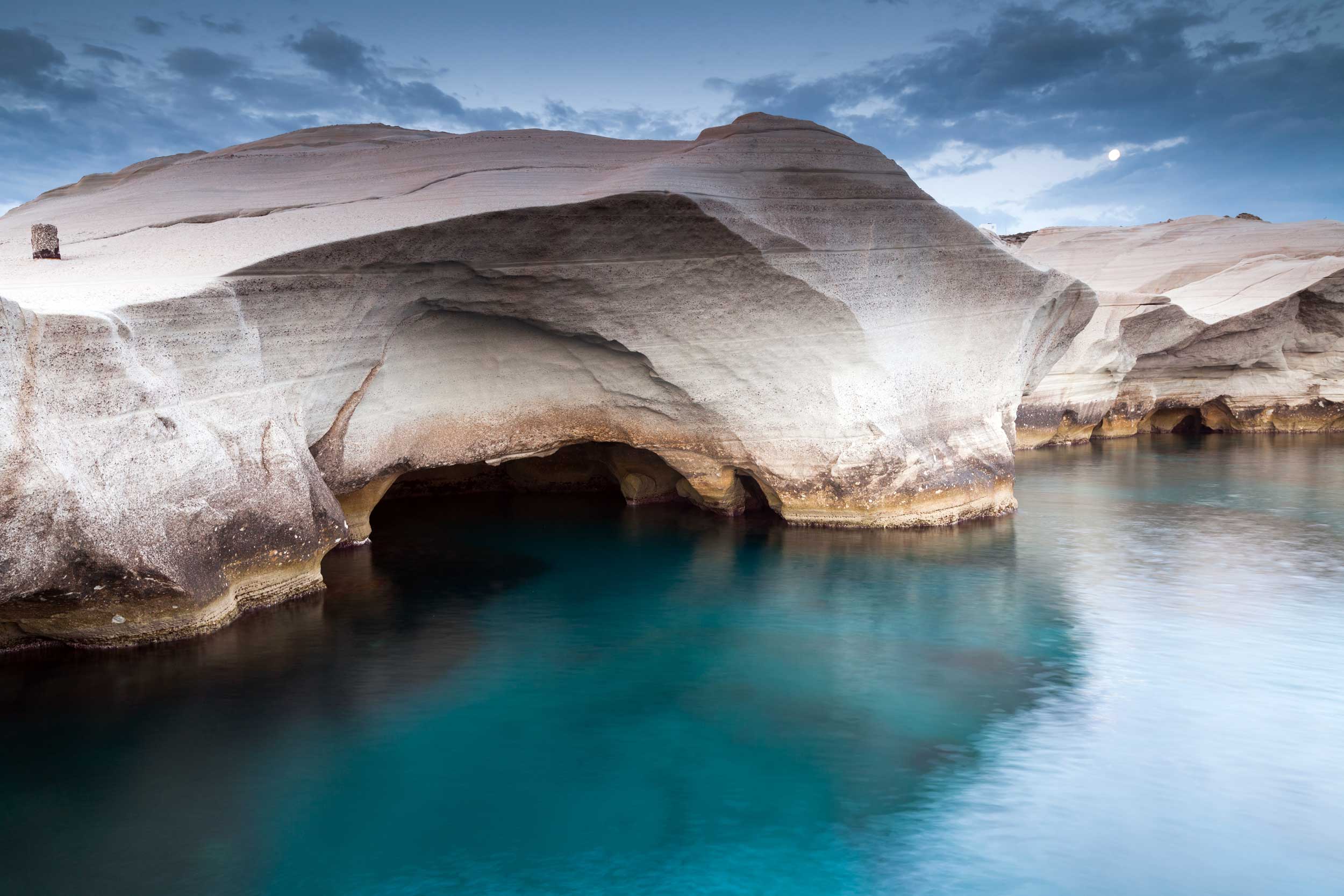 Flat whitish rock arched over a deep aquamarine sea forming a cave, Greece