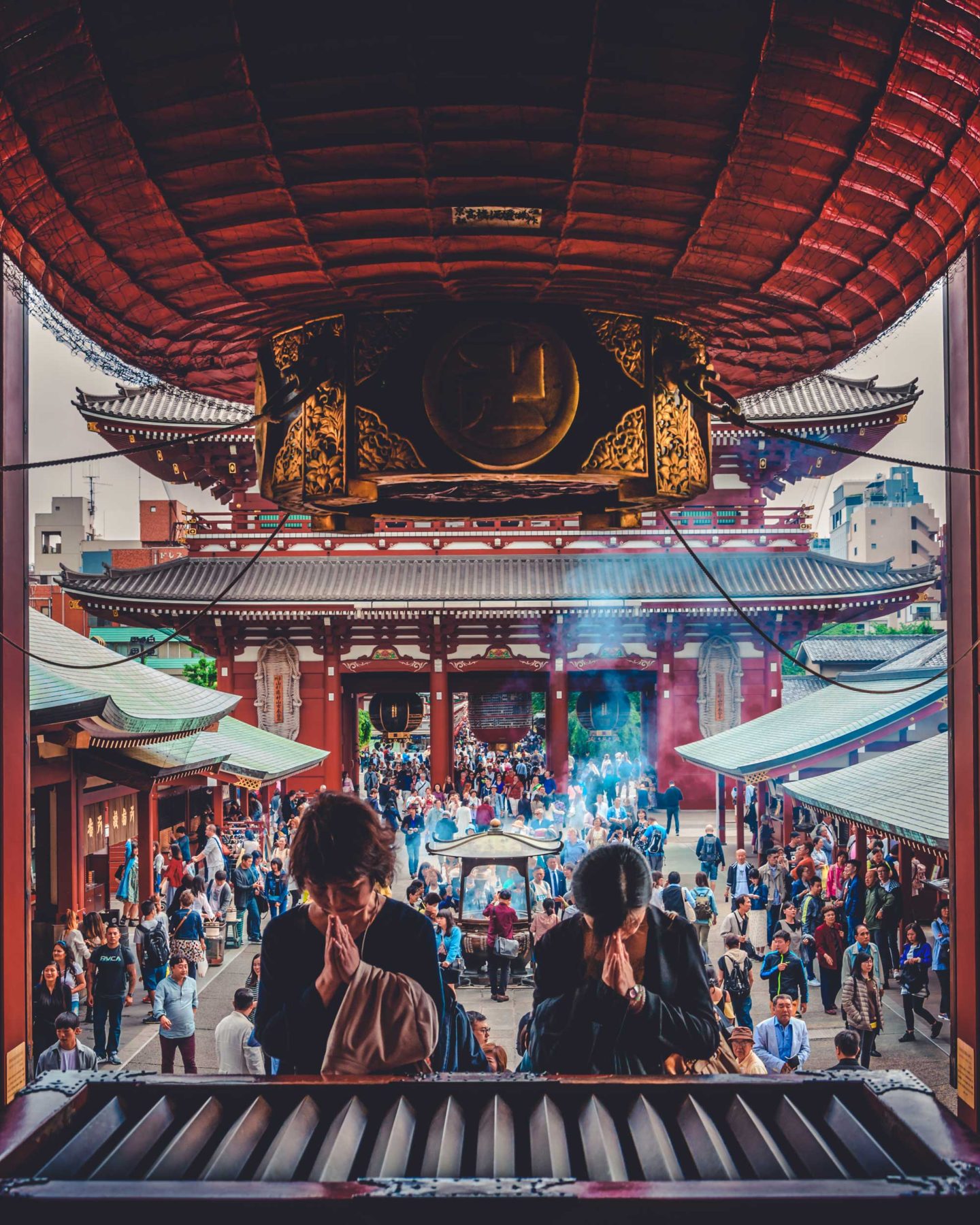 Two women praying at an altar under a red roof, above the bustling crowd on the street below, Tokyo