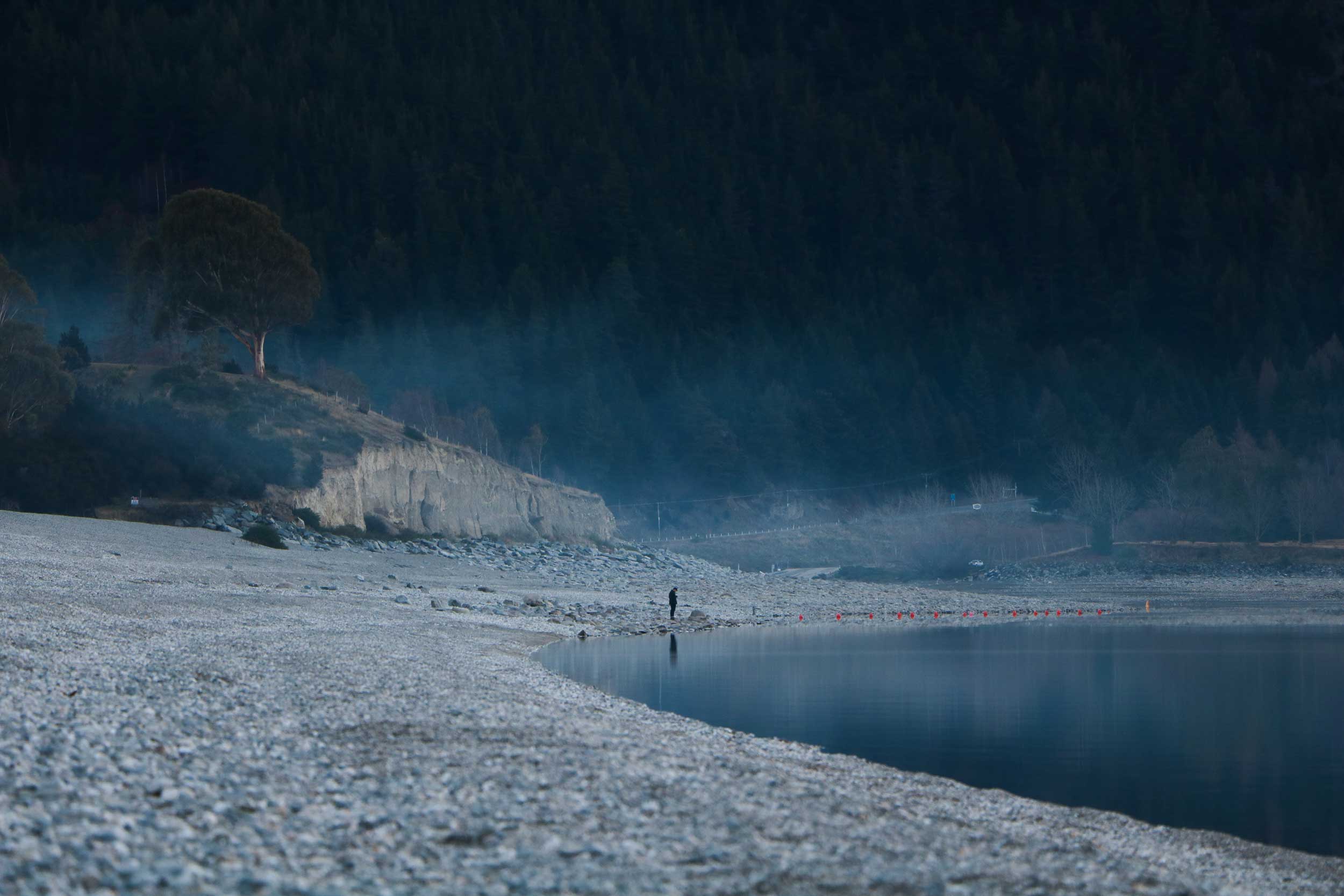 Man standing on a vast stony bank right at the edge of the lake's water, New Zealand