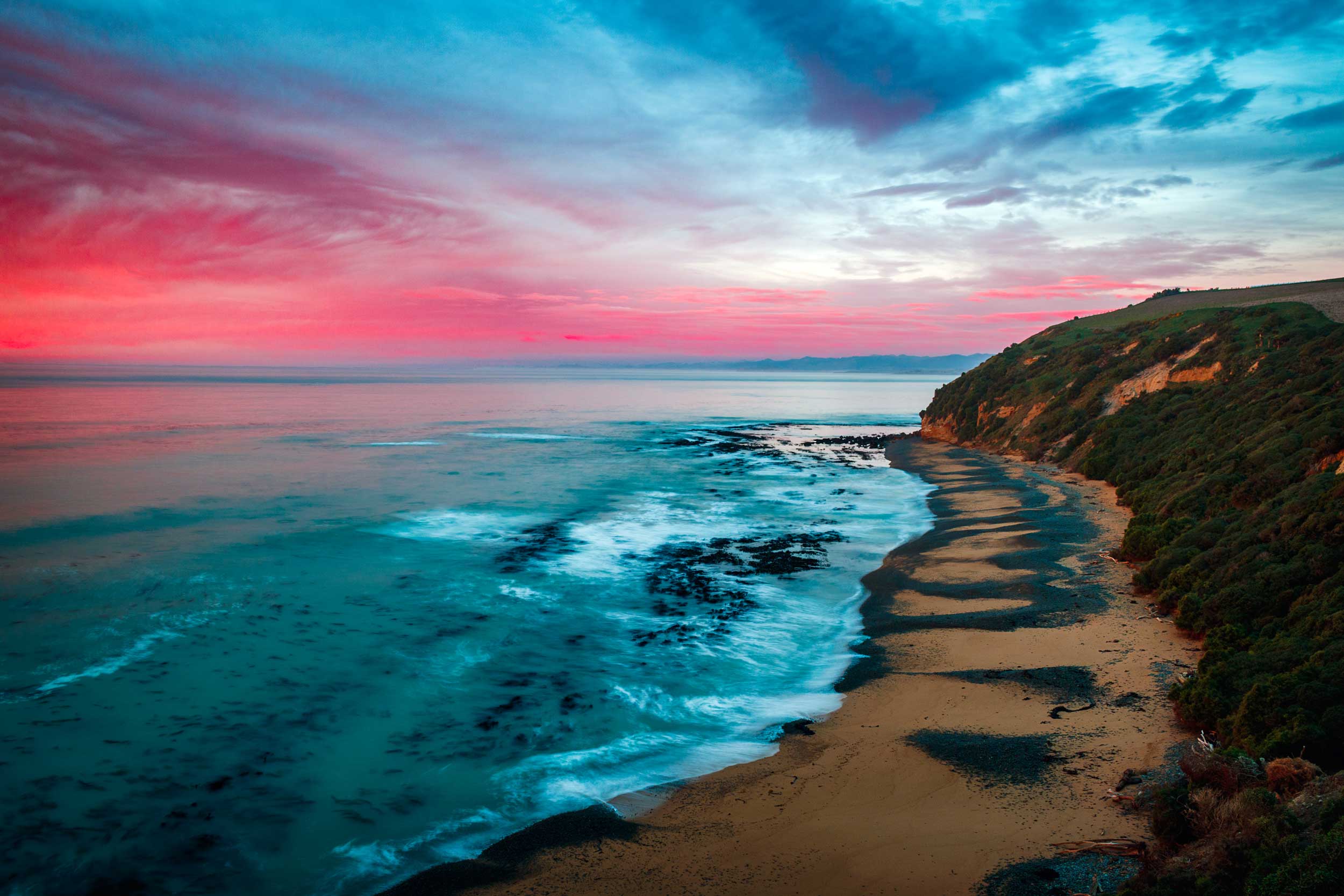 Sea lapping a sandy beach with a sunset red sky, New Zealand