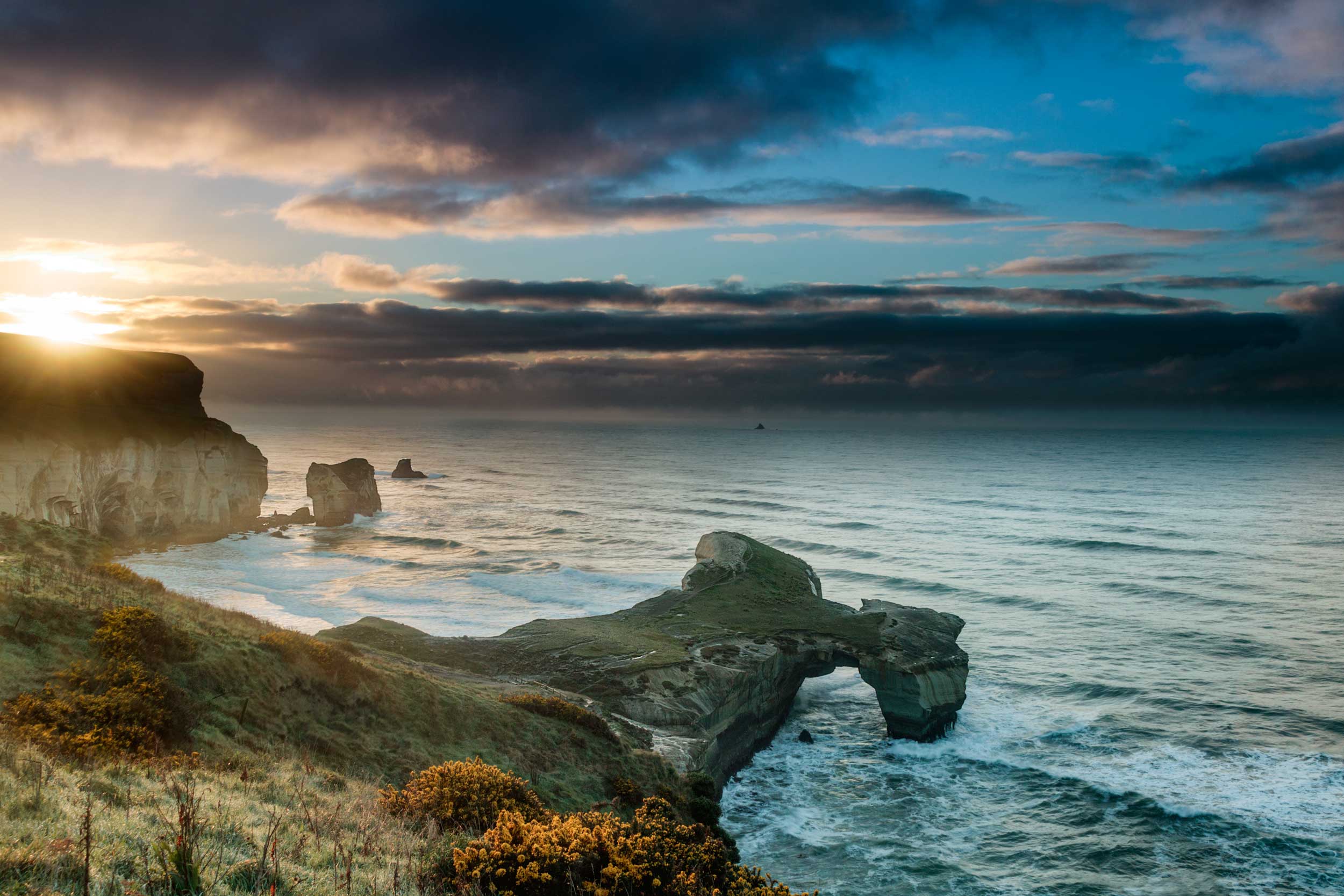 A promontory stretching out to sea with an archway at the end and the sun setting, New Zealand