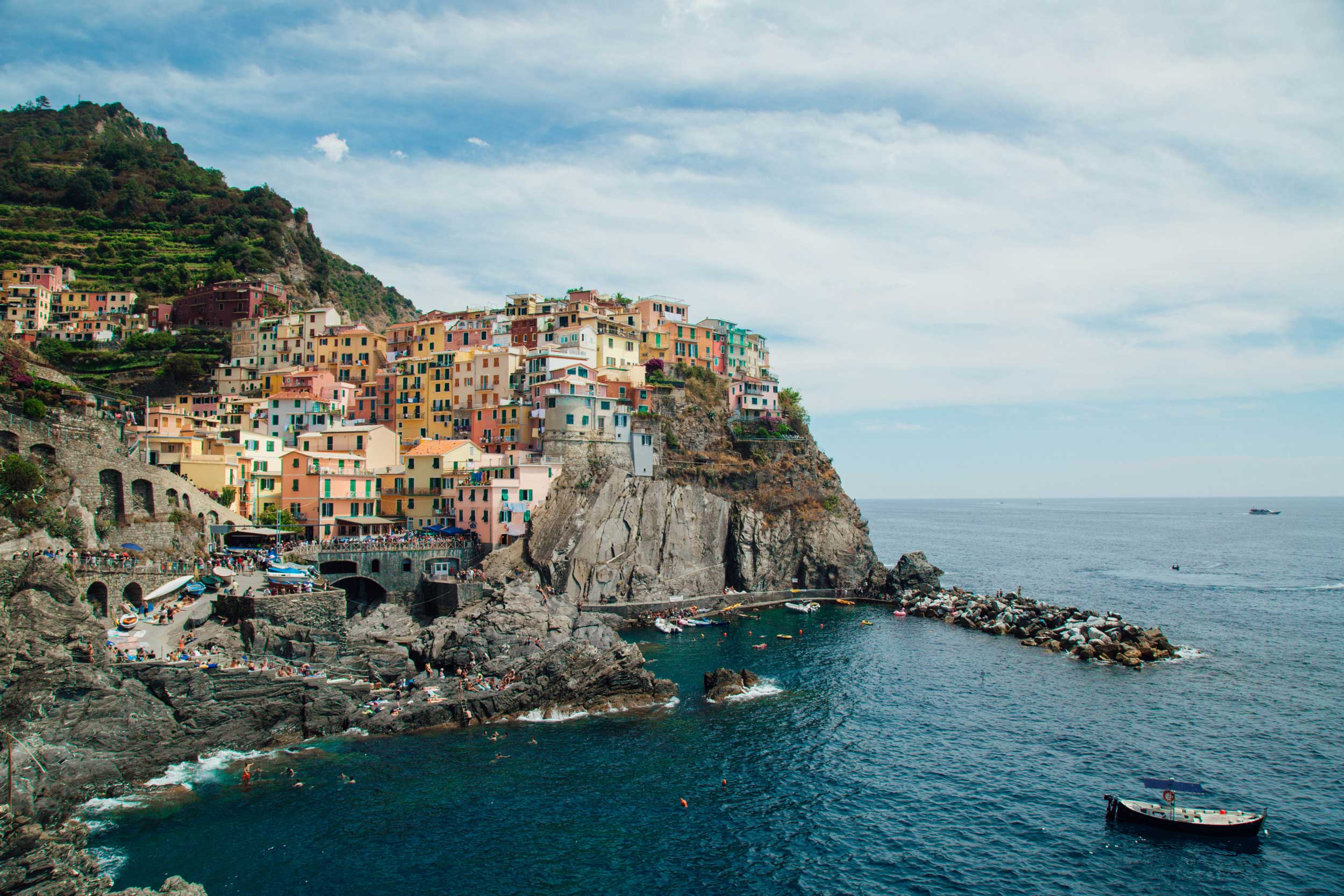 A town with multi-coloured buildings perched on a cliff with people swimming in the sea, Cinque Terre, Italy