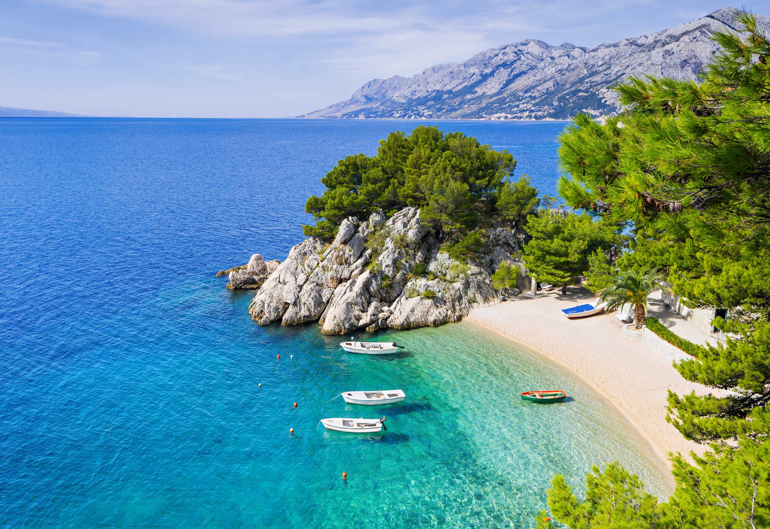 A small, sandy beach with four boats moored in clear blue water by it, Croatia