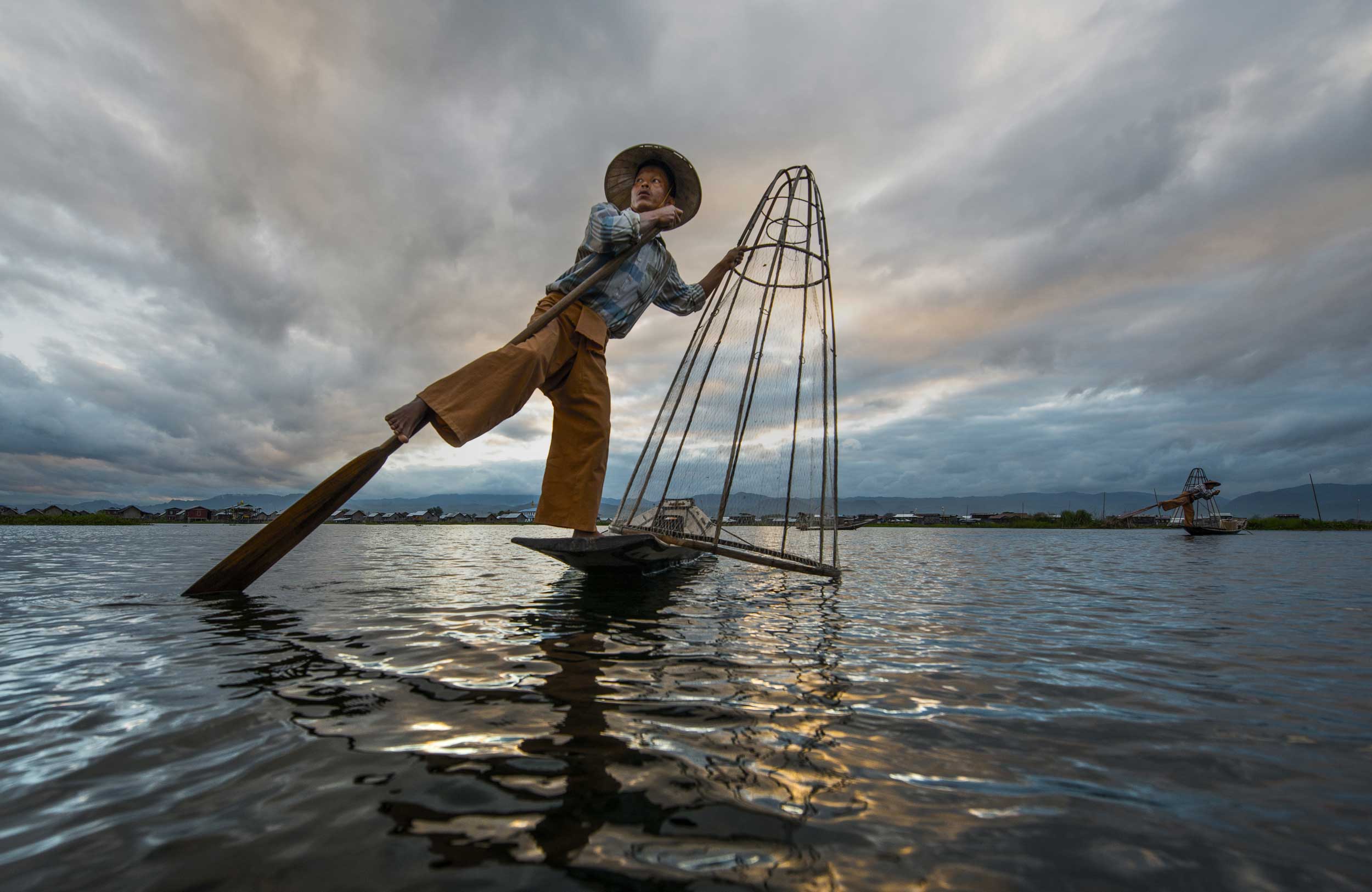Fisherman balanced on one foot while paddling with the other in Myanmar
